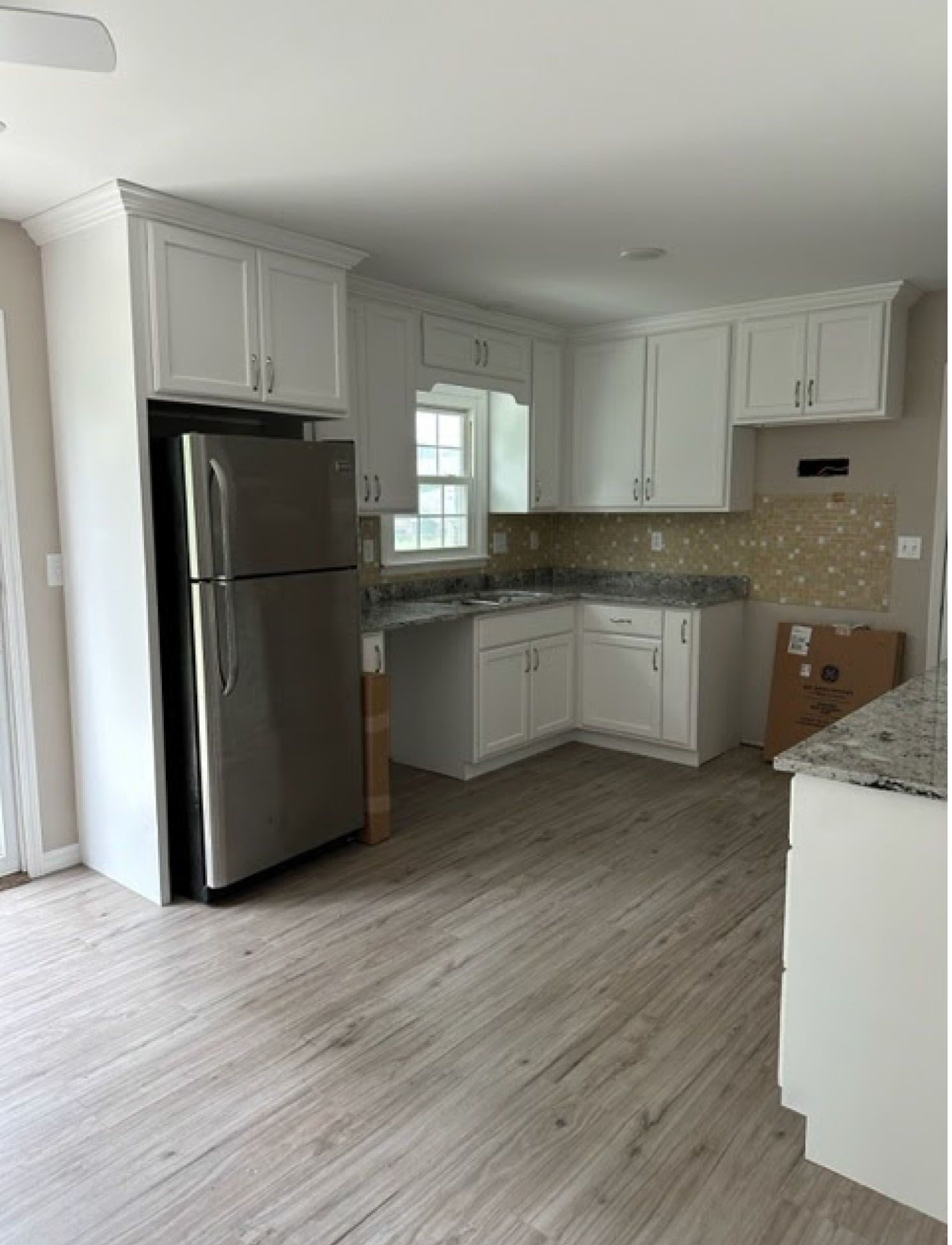 White kitchen with stainless steel refrigerator, white cabinets, and light wood-look flooring.
