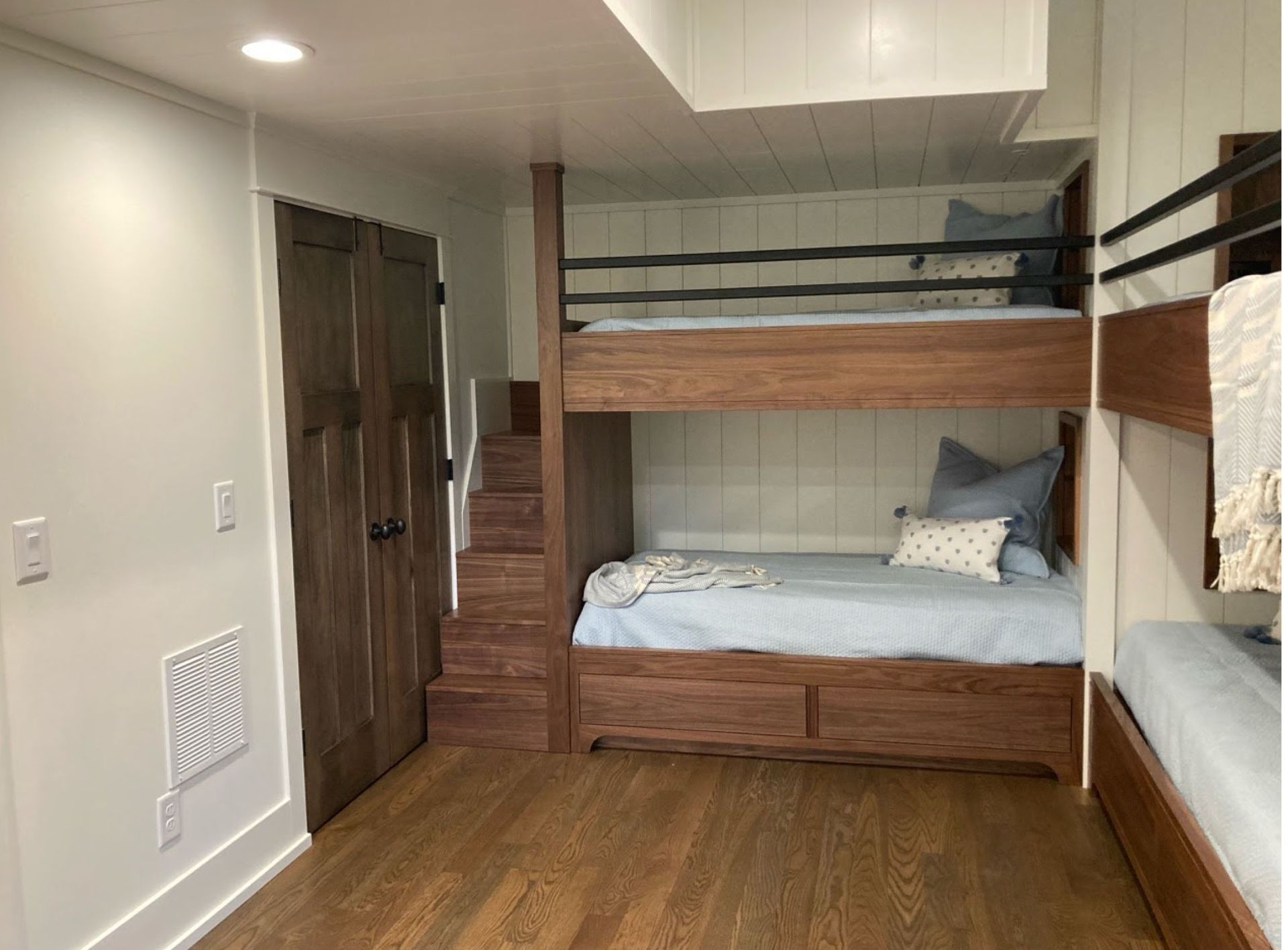 Wooden bunk beds in a room with wood flooring and white walls. Includes a doorway and small staircase.