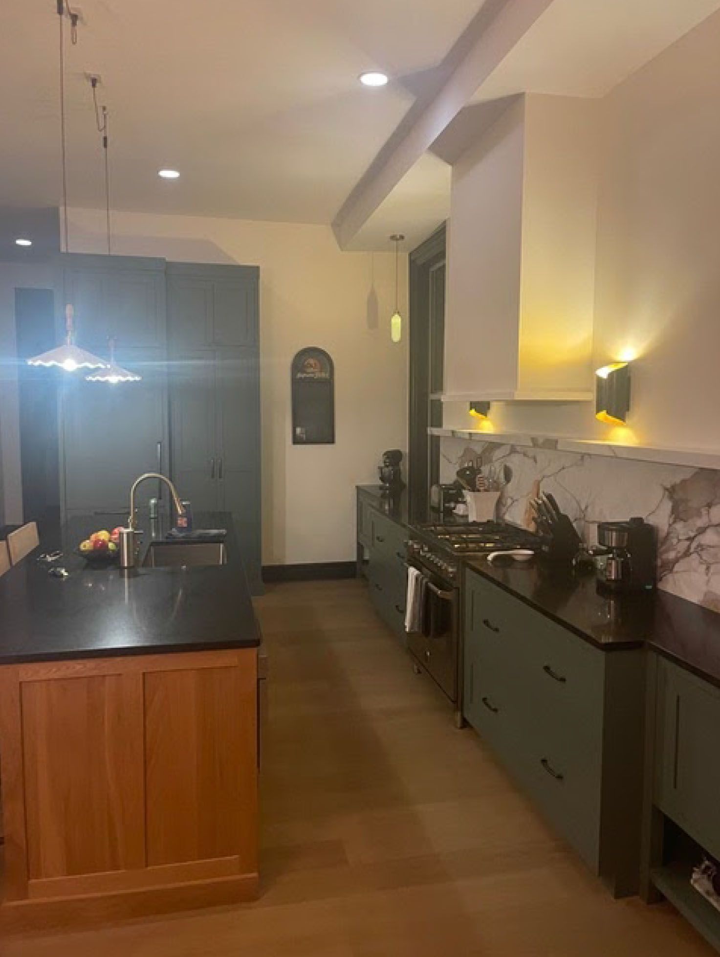 Kitchen with dark green cabinets, wood island, and marble backsplash.