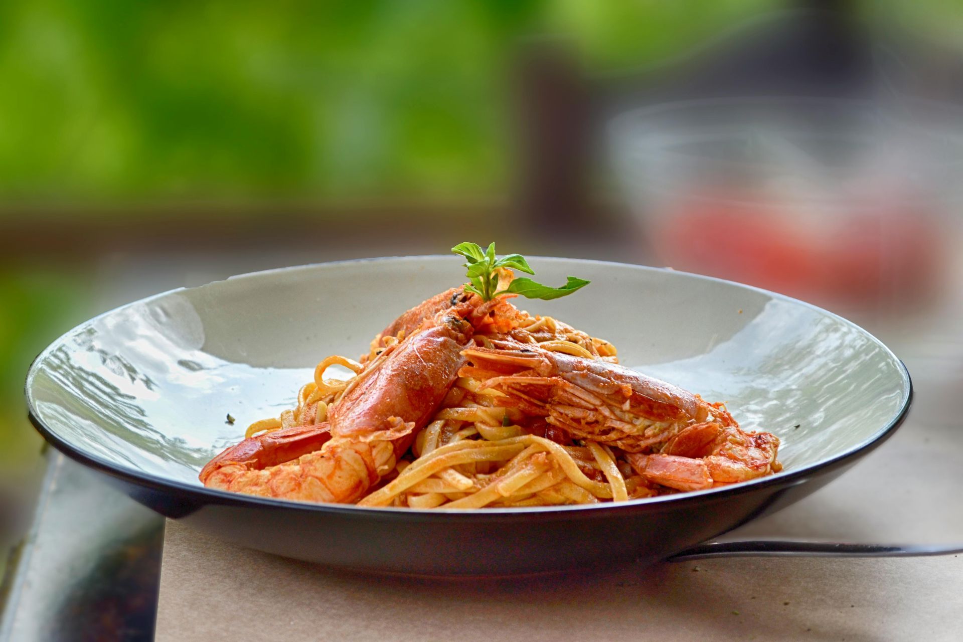 Pasta with shrimp in a white and grey bowl, with greenery in the background.