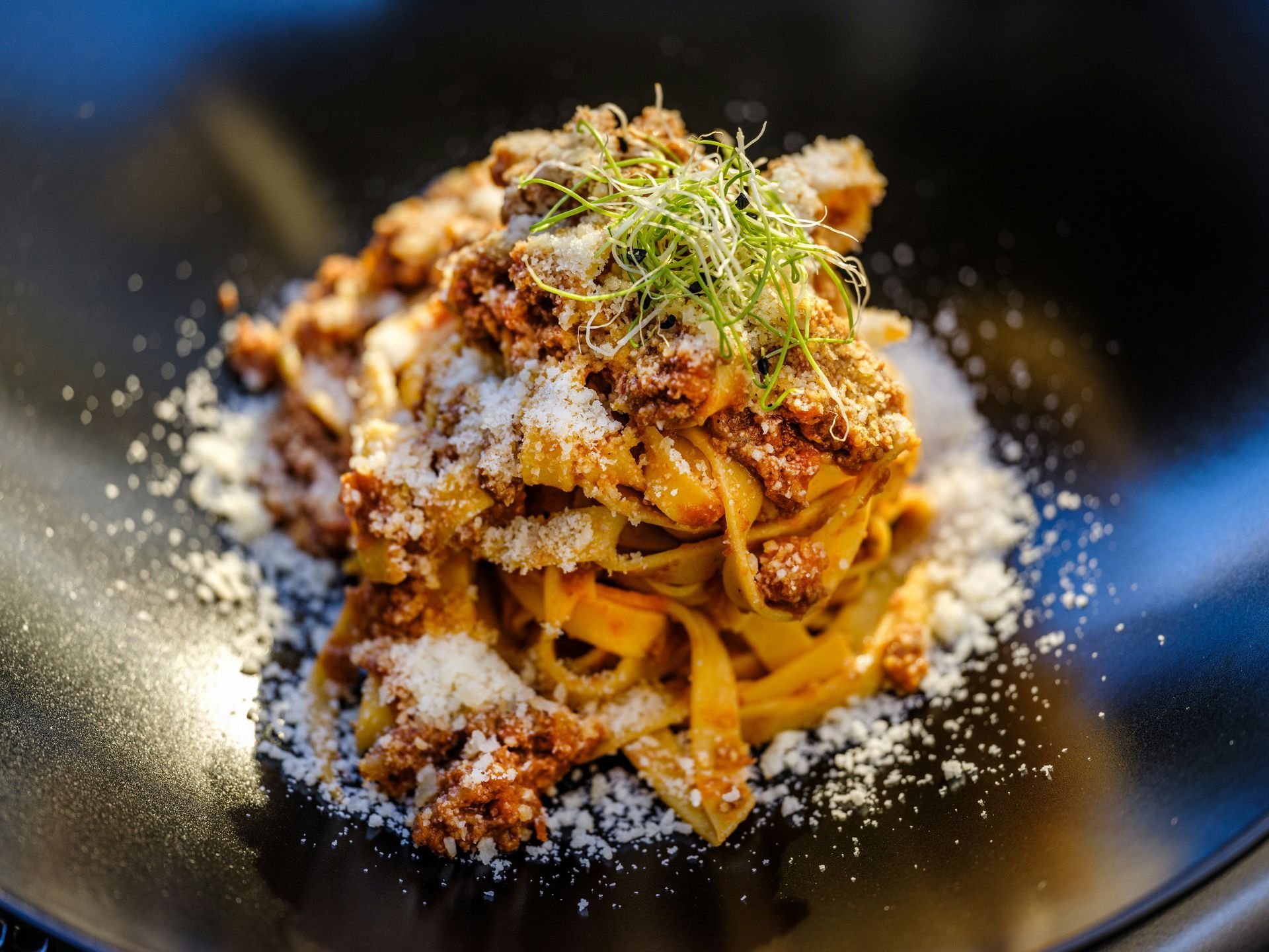 Pasta with meat sauce, grated parmesan cheese, and herbs on a black plate.