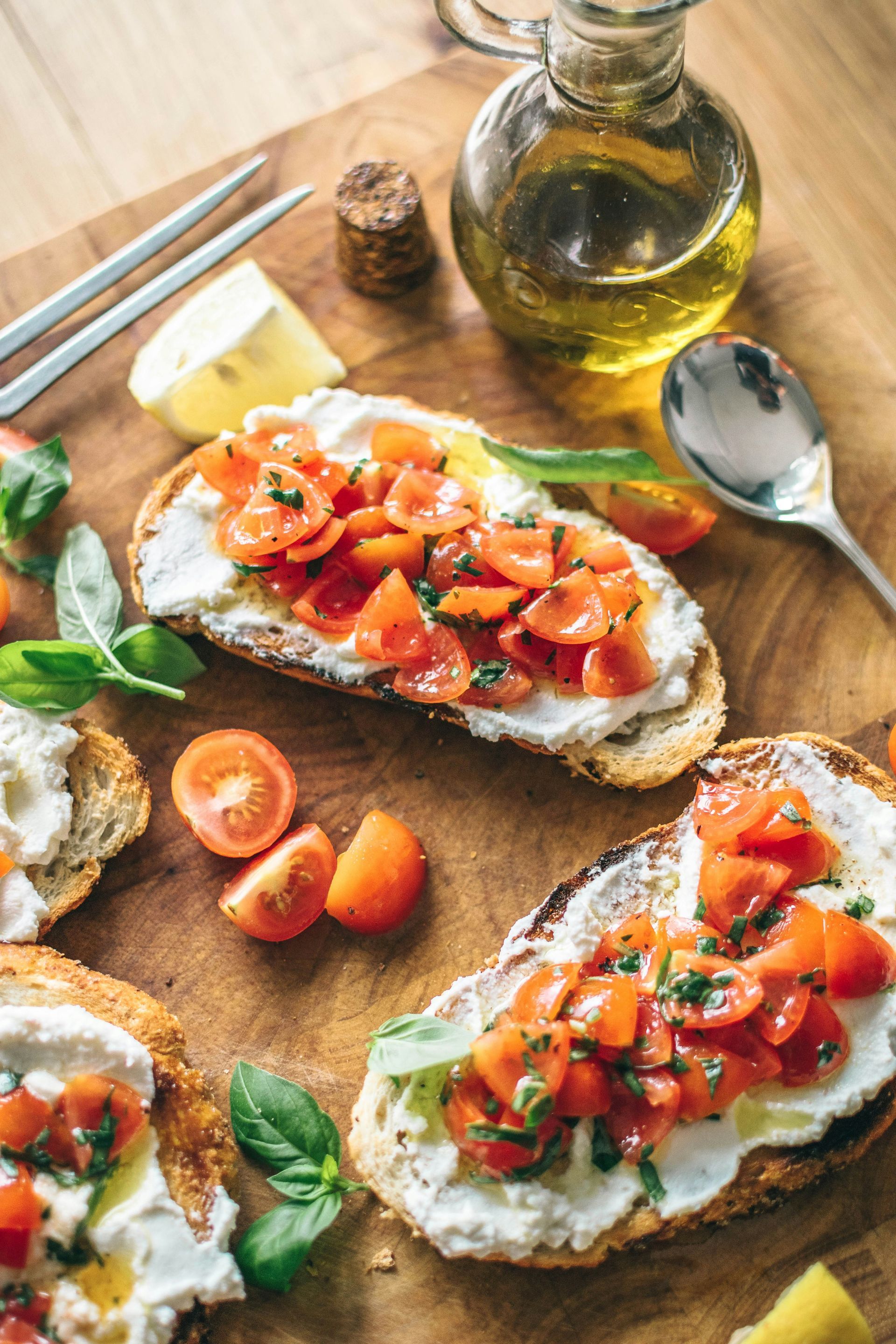 Bruschetta on a wooden board with cherry tomatoes, ricotta cheese, basil, and olive oil.
