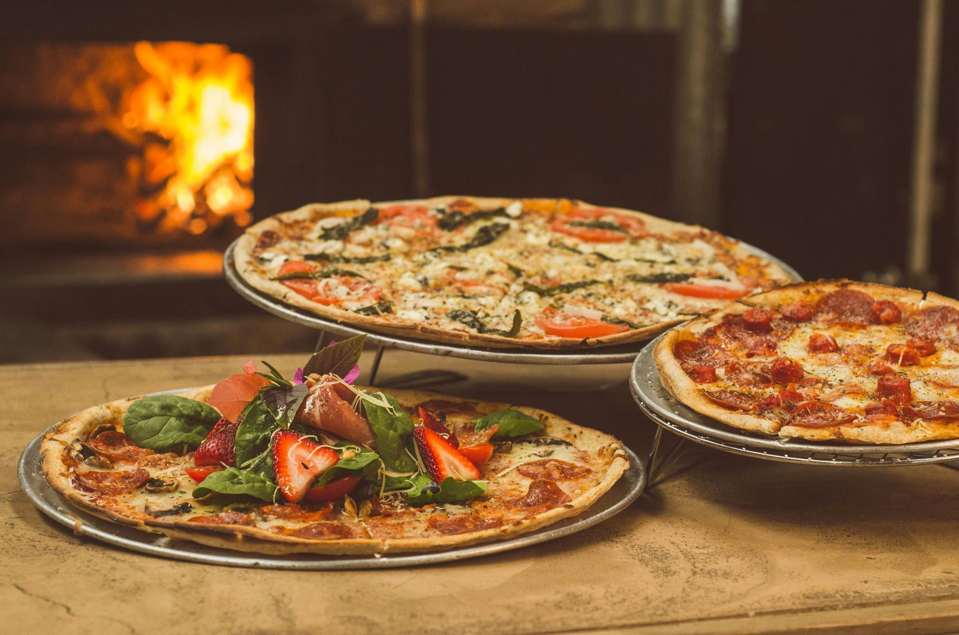 Three pizzas on metal stands, in front of a wood-fired oven.