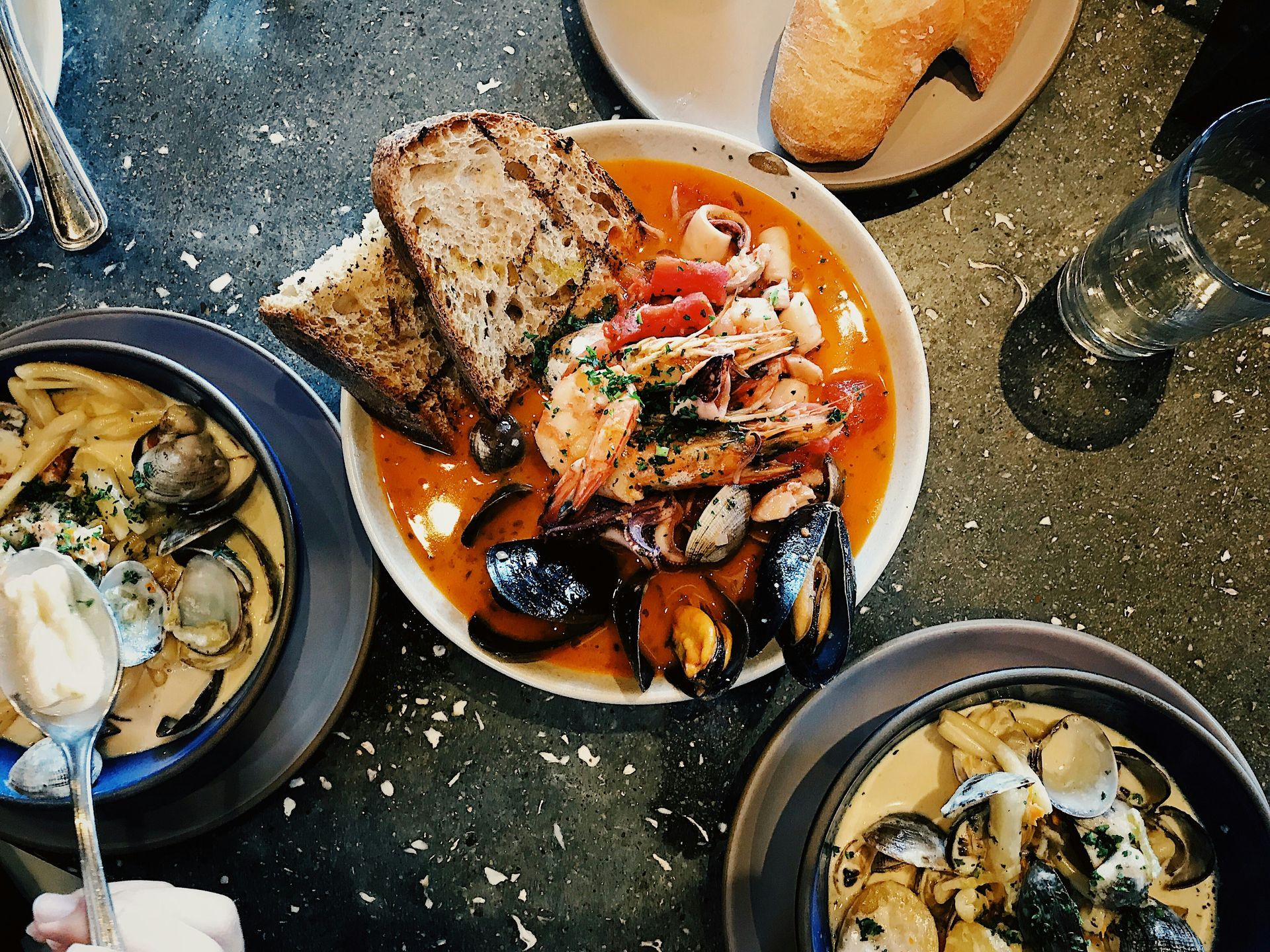 Seafood stew with bread, surrounded by bowls of creamy soup, on a speckled table.