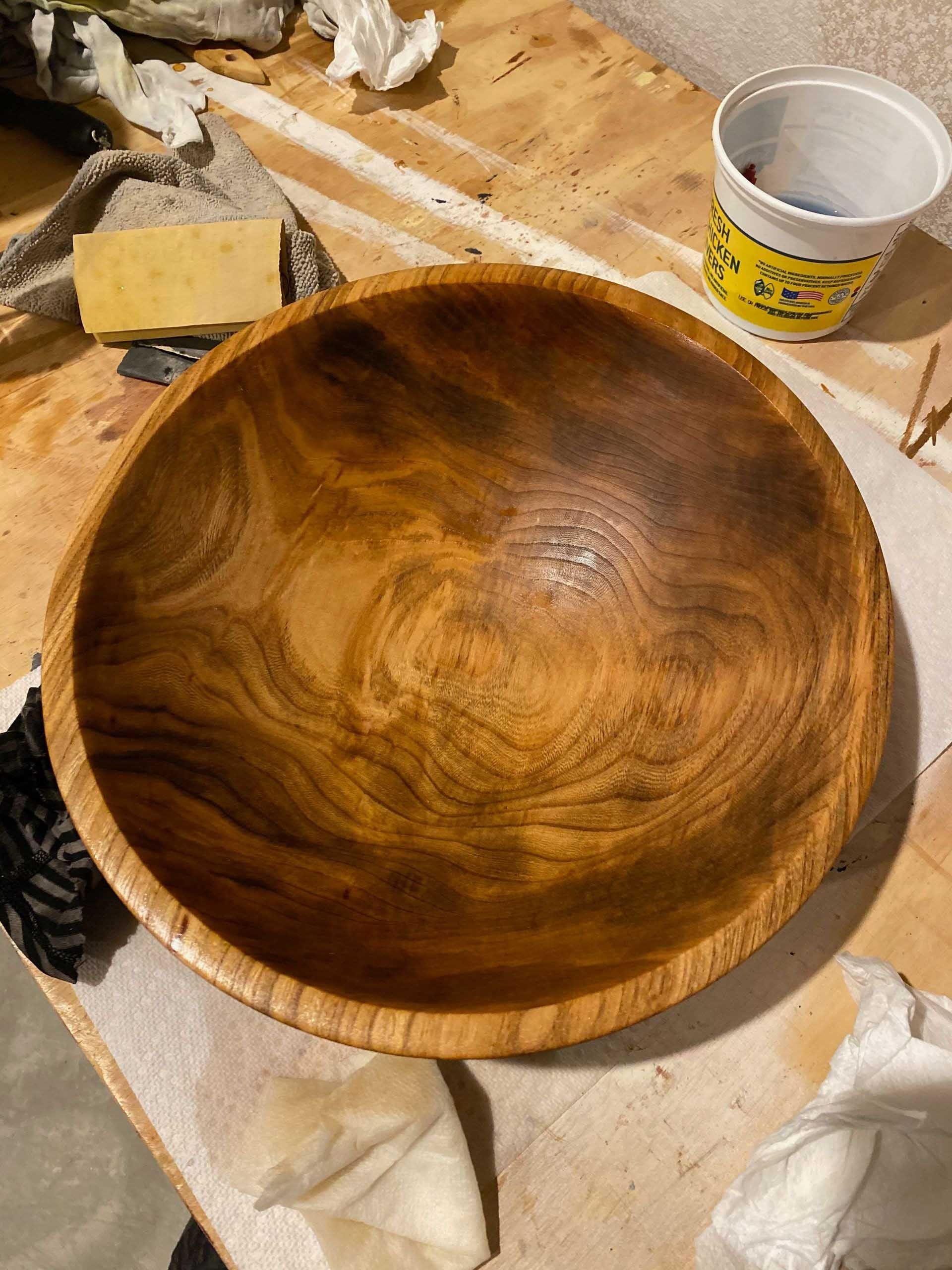 Wooden bowl with rich, swirling grain patterns in shades of brown and tan, resting on a work surface.