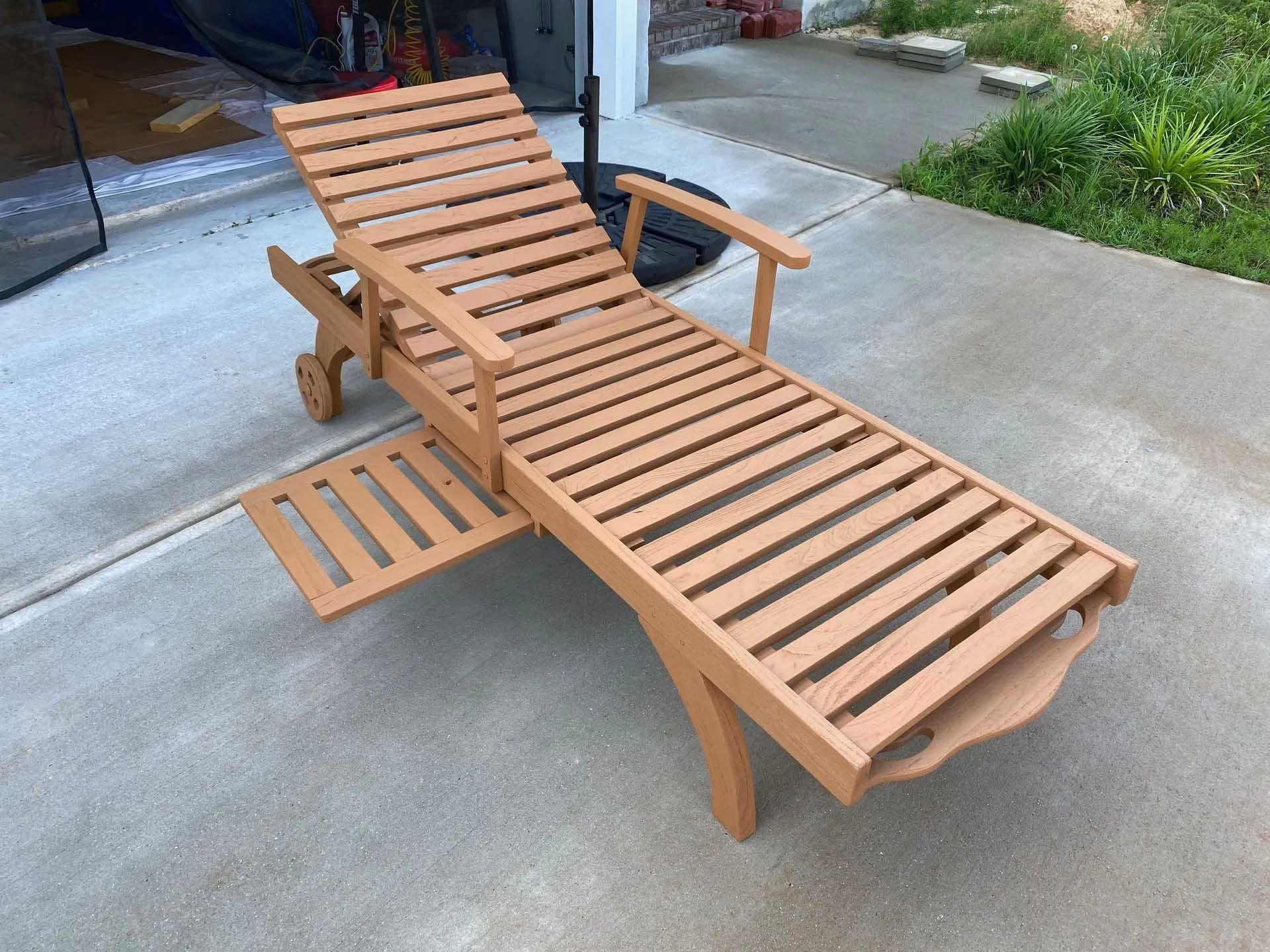 Brown wooden outdoor chaise lounge chair on a concrete driveway, with attached side table and wheels.