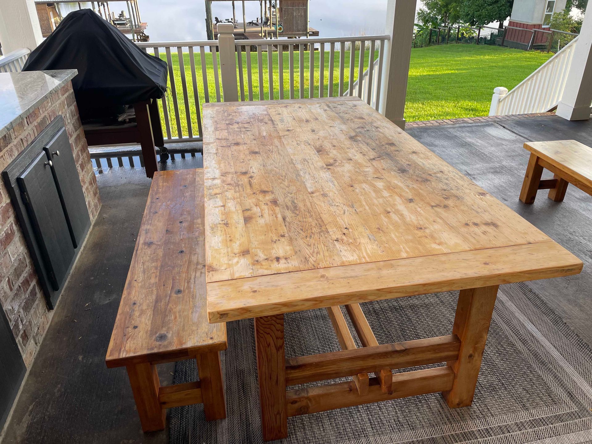 Wooden outdoor dining table and bench on a patio overlooking a body of water.