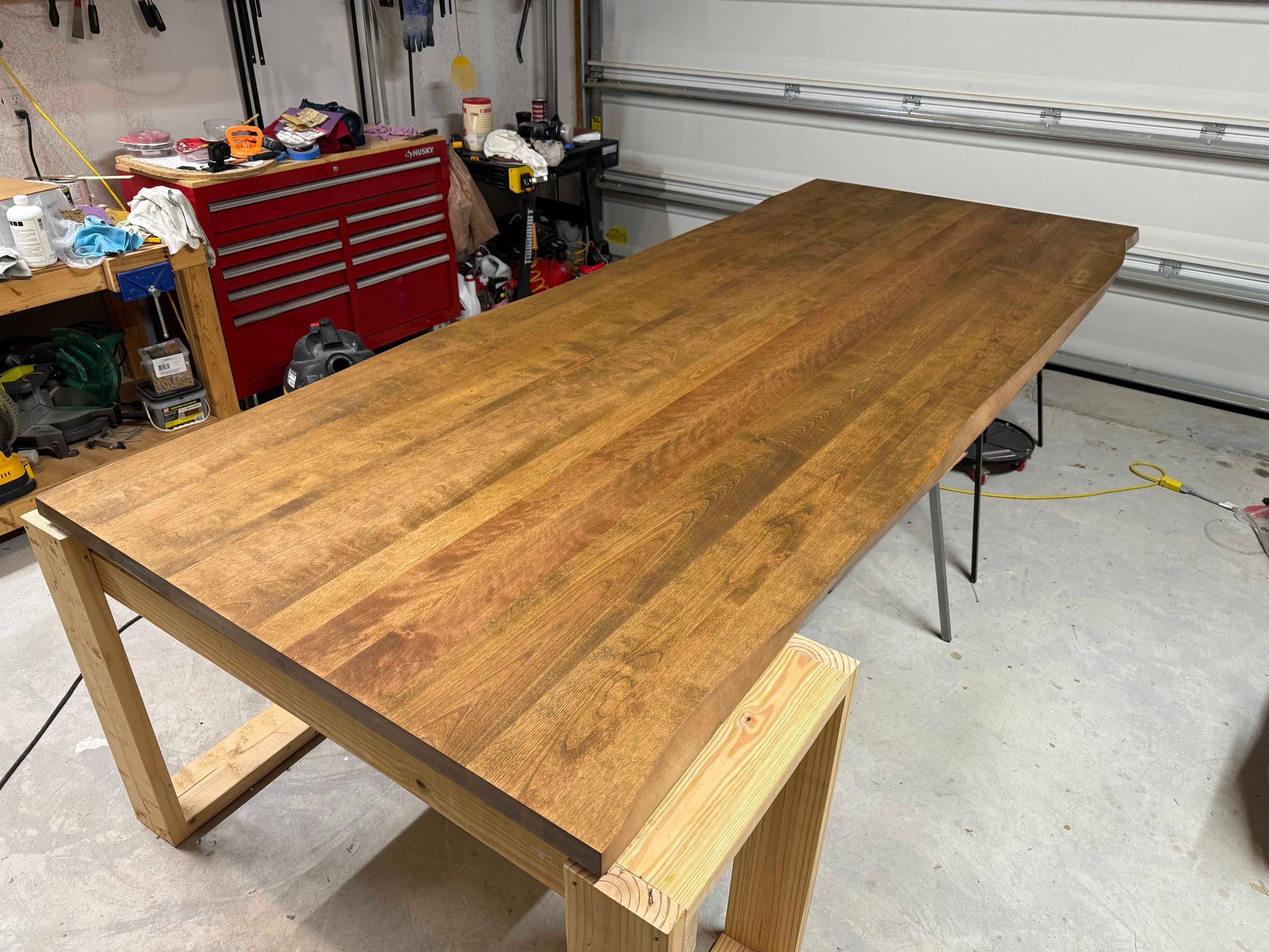Wood tabletop on a wooden frame, in a garage. Tools and storage in background. Brown stained wood.