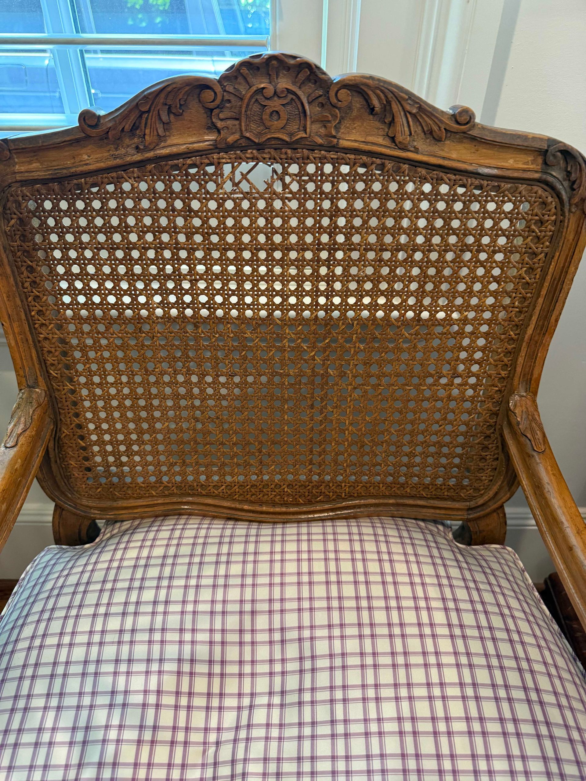 Wooden chair with caned back, ornate carving, and checkered cushion.