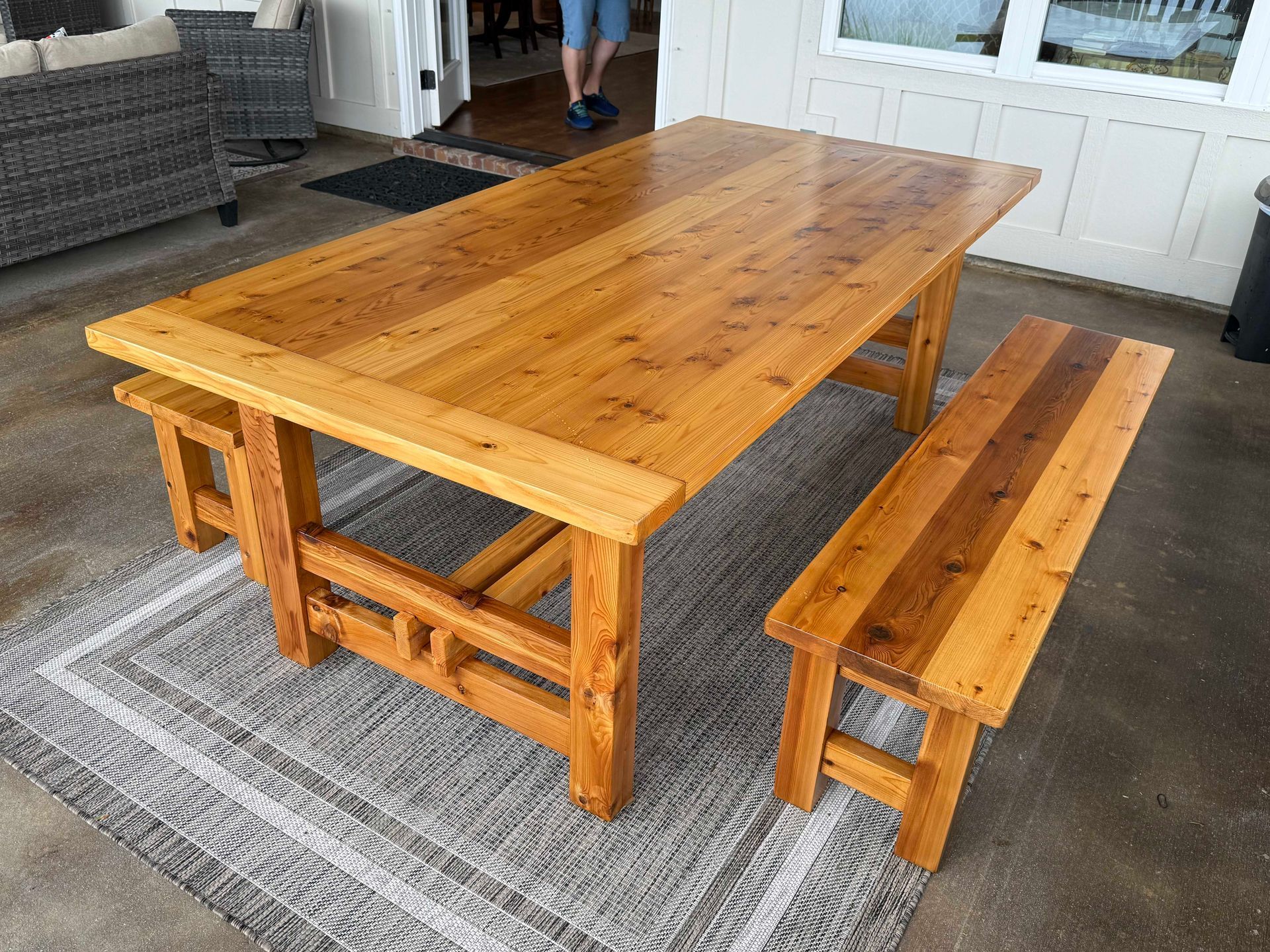 Wooden dining table and bench set on a gray outdoor rug.