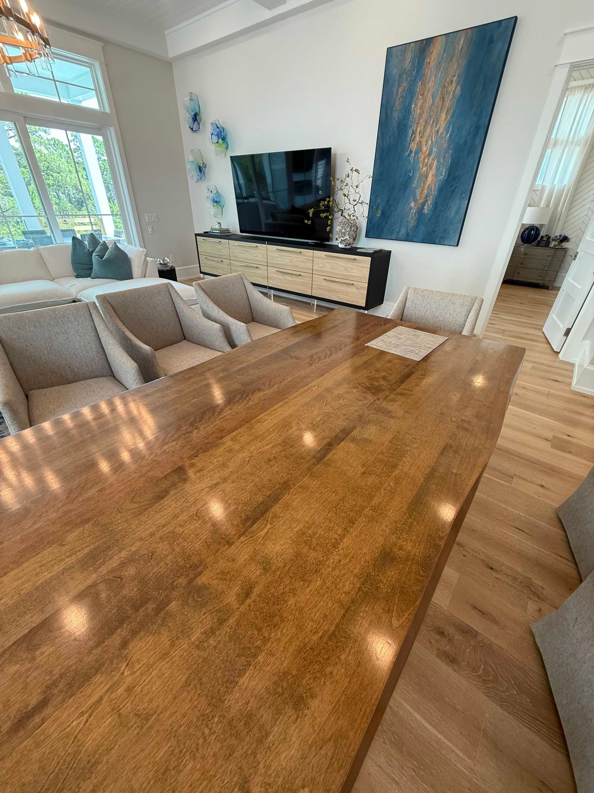 Spacious, modern kitchen with a large wooden island and a TV against a white wall; light-filled setting.