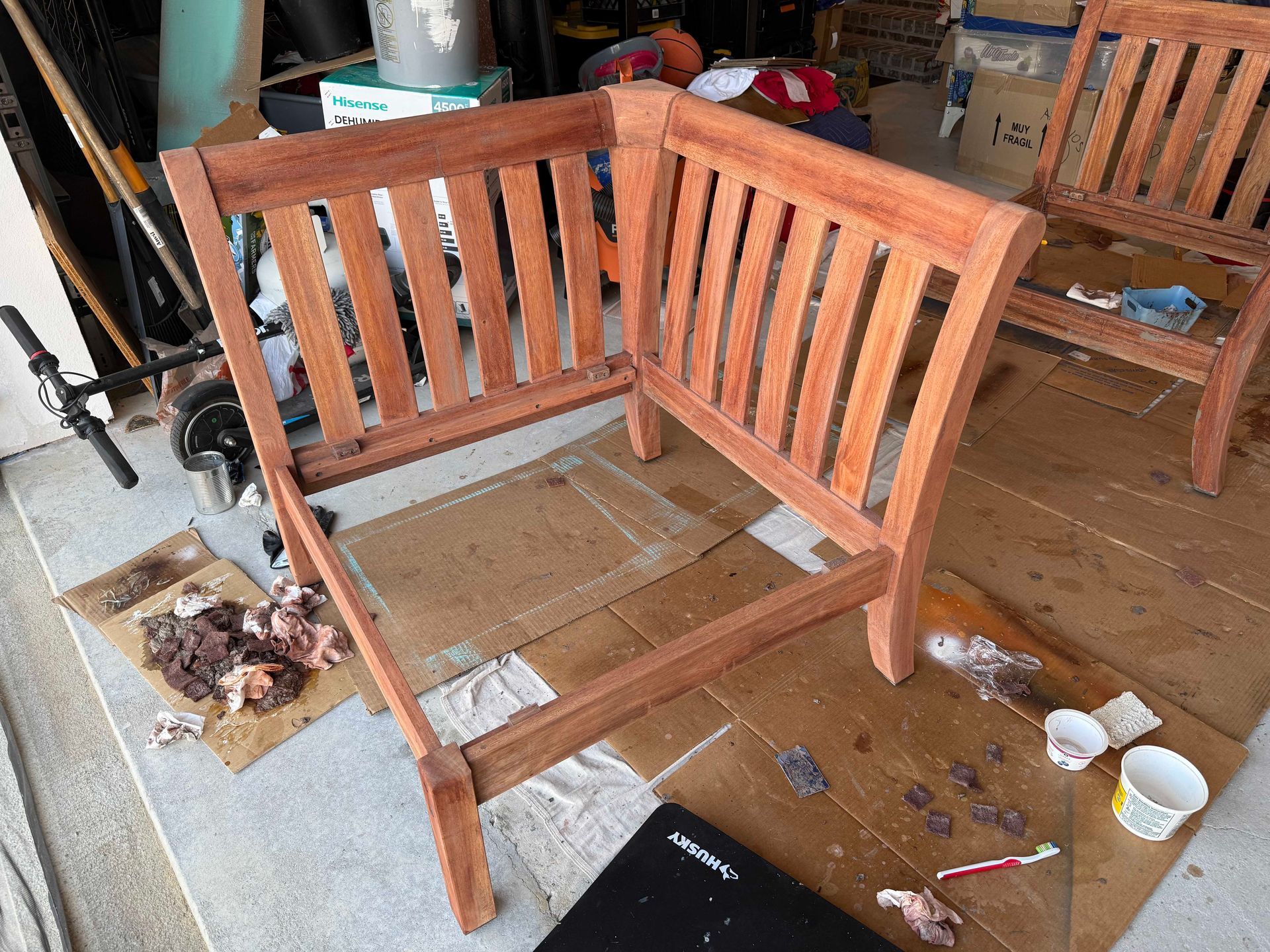 Wooden outdoor chair frame being refinished outdoors on a concrete surface.
