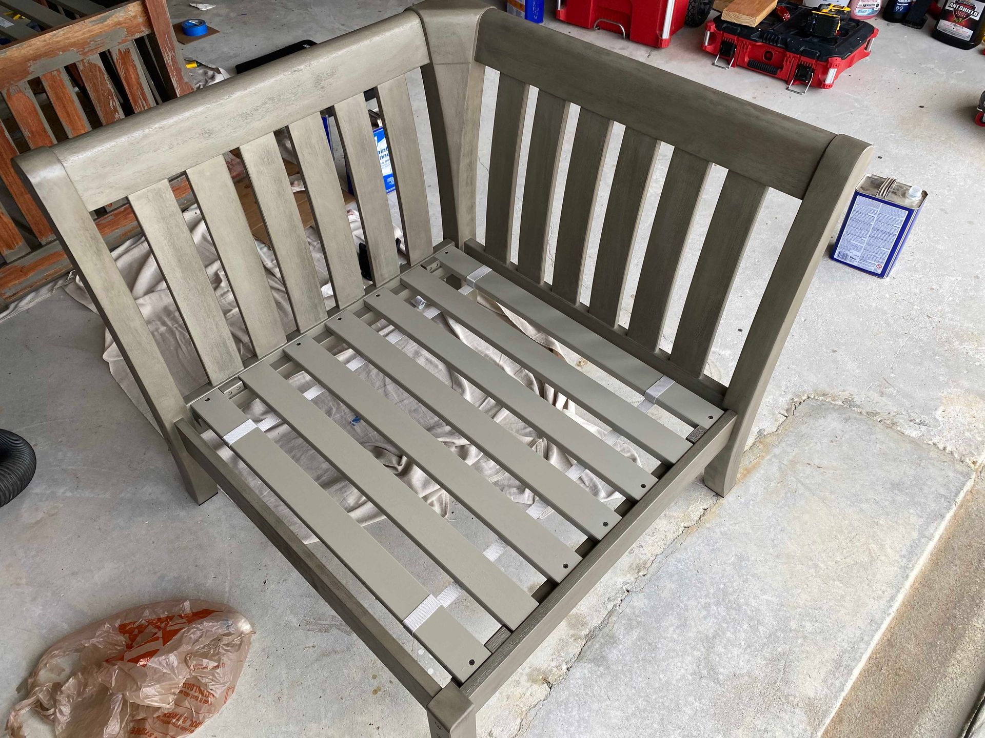 Gray painted corner outdoor bench, unfinished, on a concrete surface.