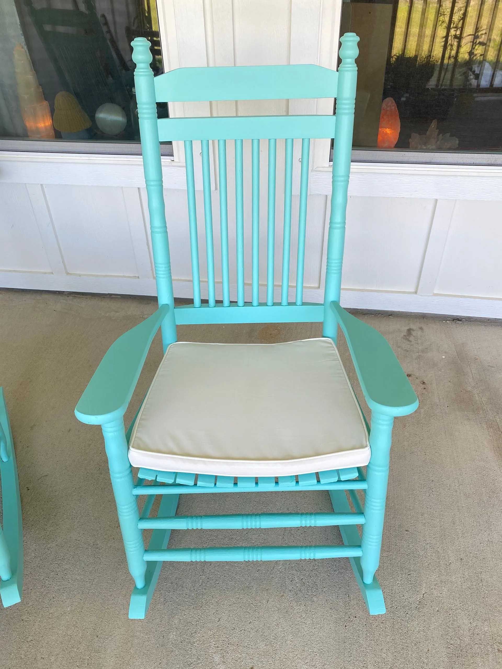 Teal rocking chair with a cream cushion on a porch.