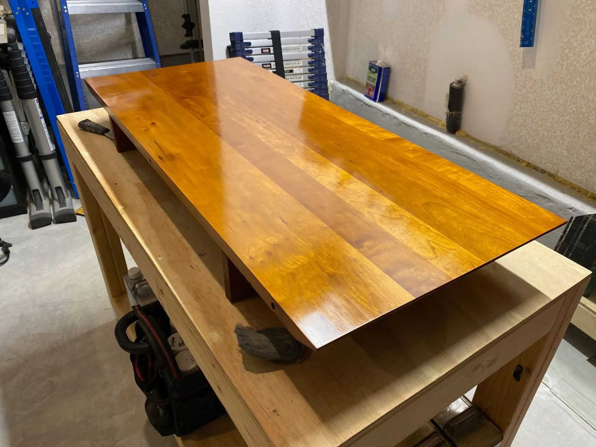Wooden tabletop being refinished in a garage workshop, resting on a workbench.