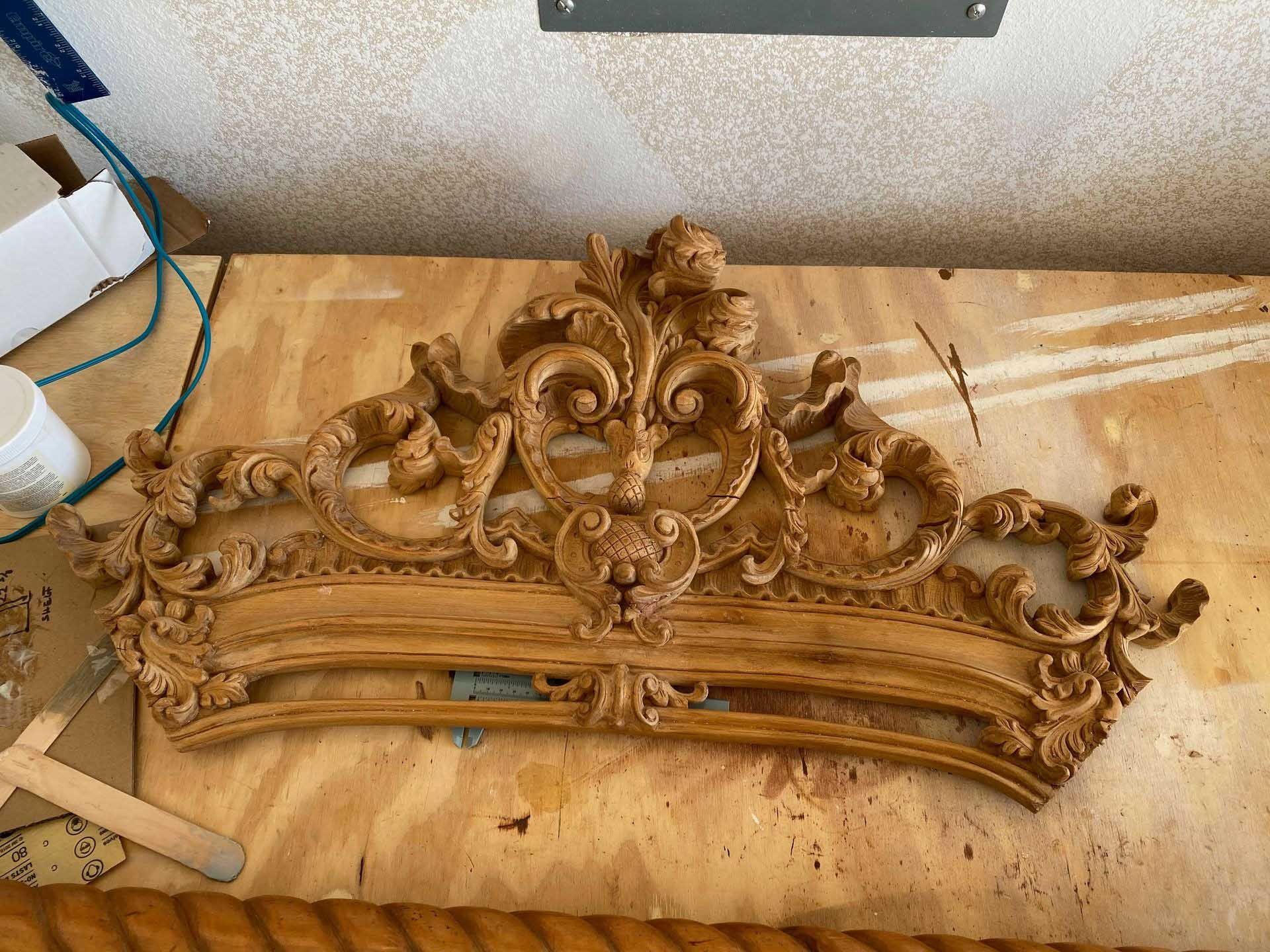 Ornate, carved wooden bed headboard in a light brown finish, lying on a wooden surface.