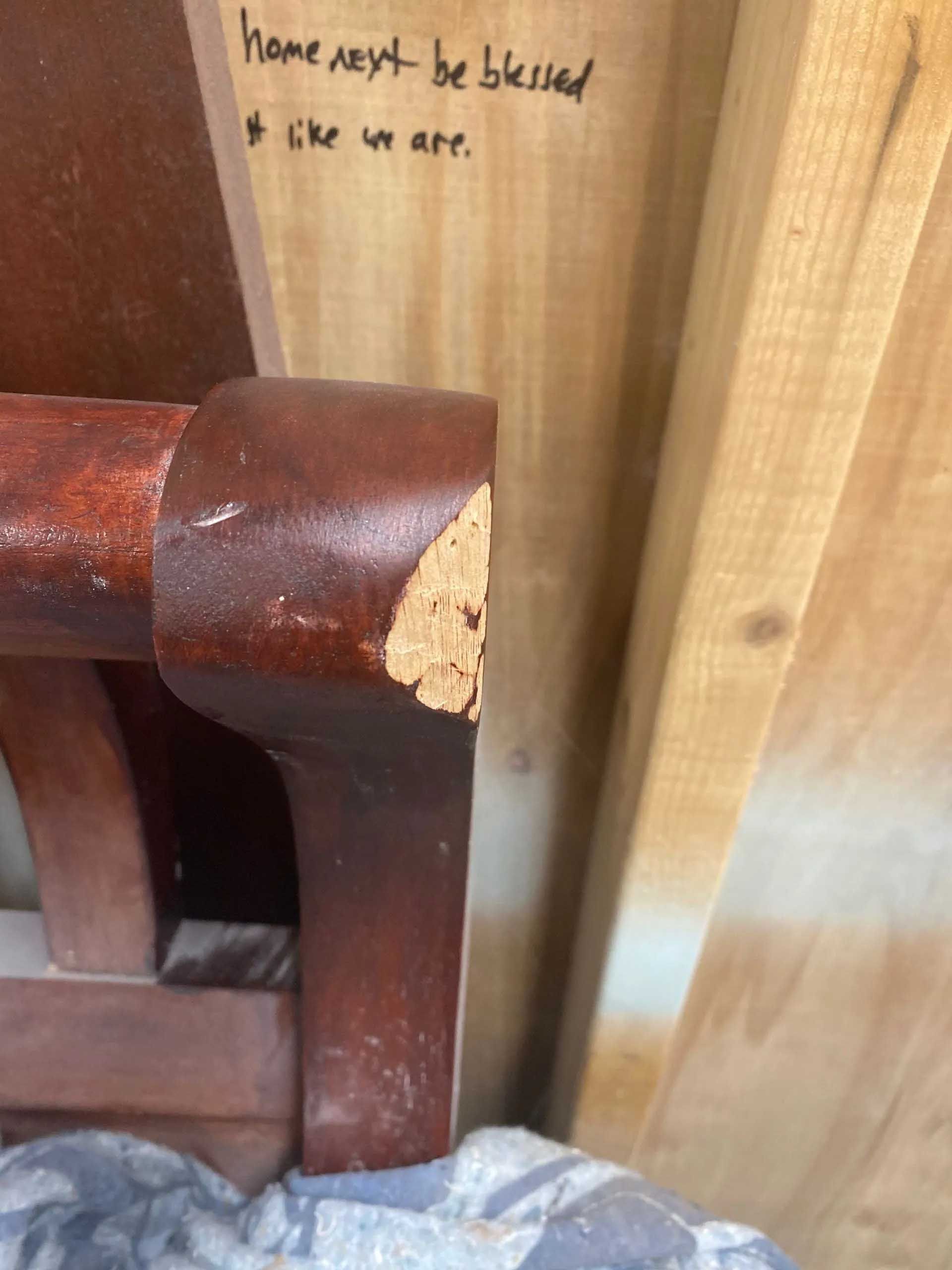 A close-up of a damaged dark red chair arm against a wooden wall, with a handwritten note that says 
