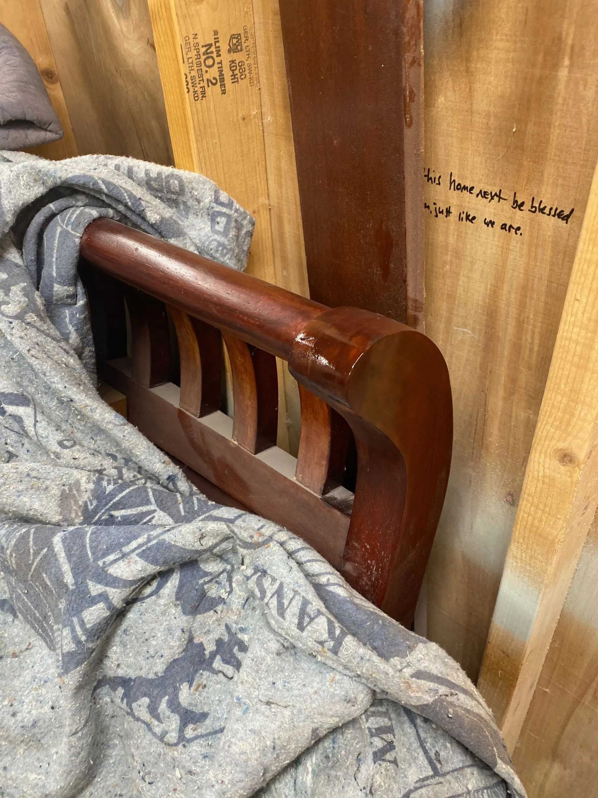 Wooden bed arm with a blanket partially covering it, set against wooden walls.