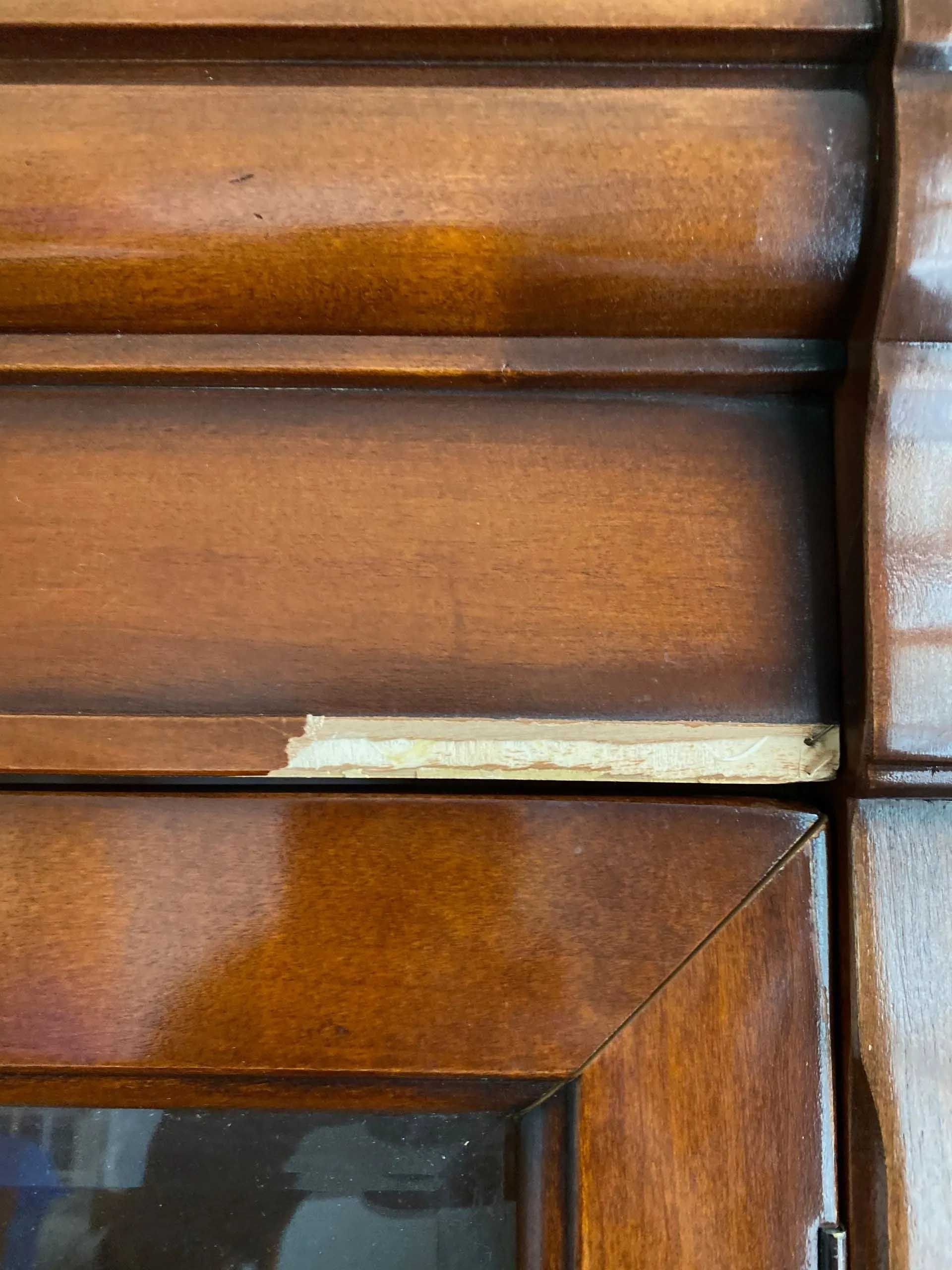 Close-up of a wooden cabinet with a chipped edge revealing a light-colored material underneath.