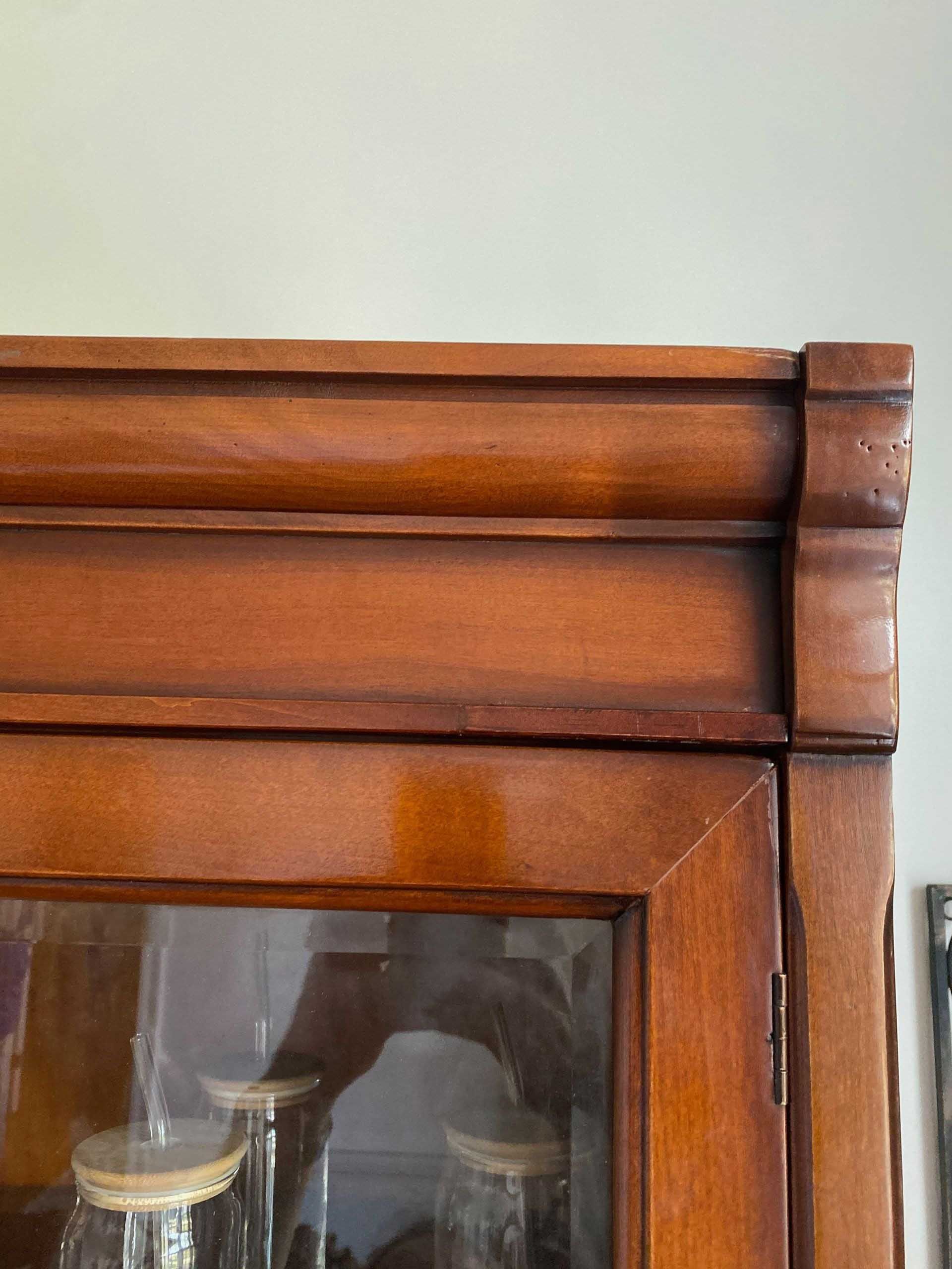 Wooden cabinet detail with a glass door, shelves, and ornate top molding.