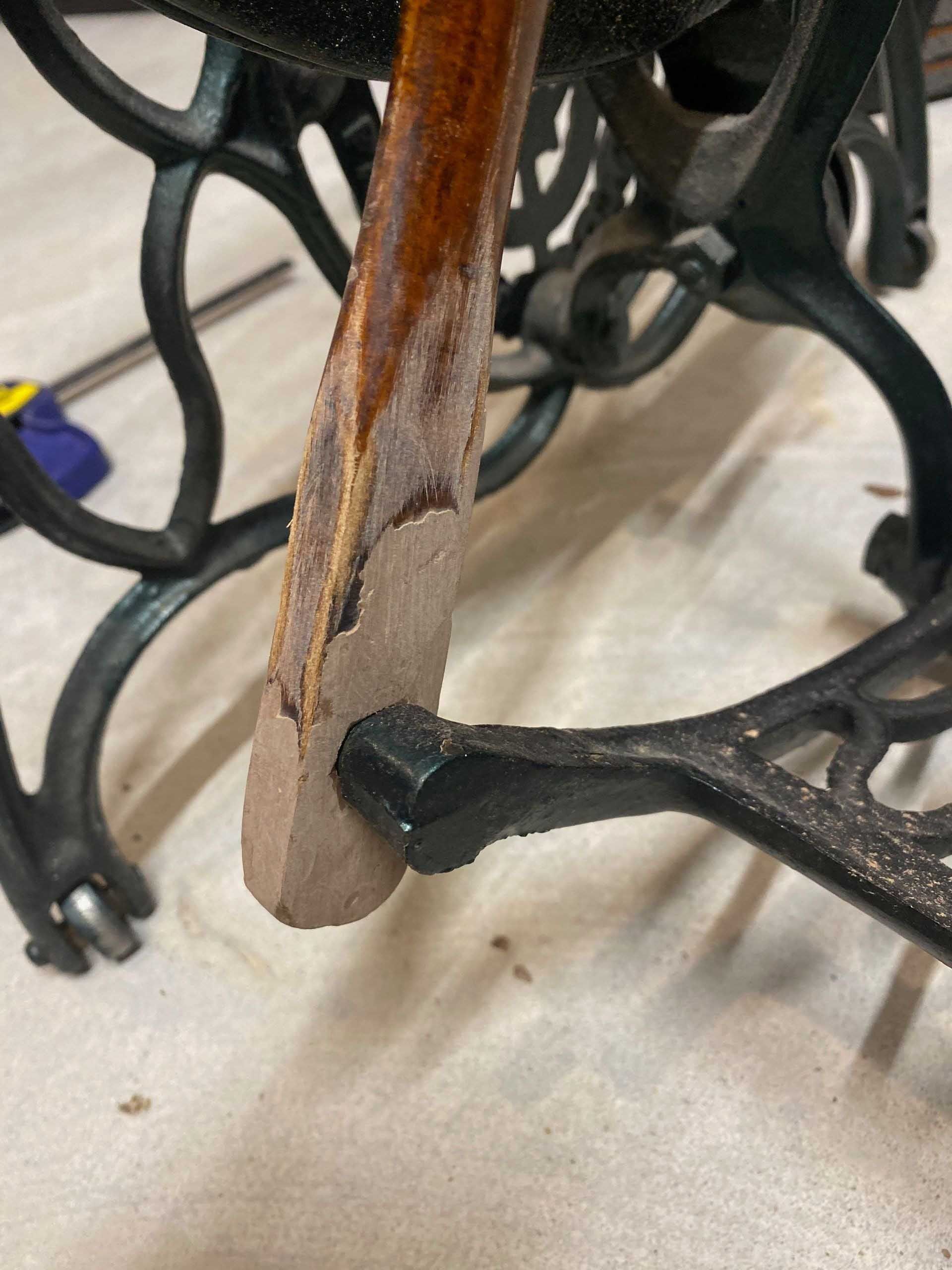 Close-up of a wooden treadle from a black antique sewing machine, showing chipped, peeling wood.
