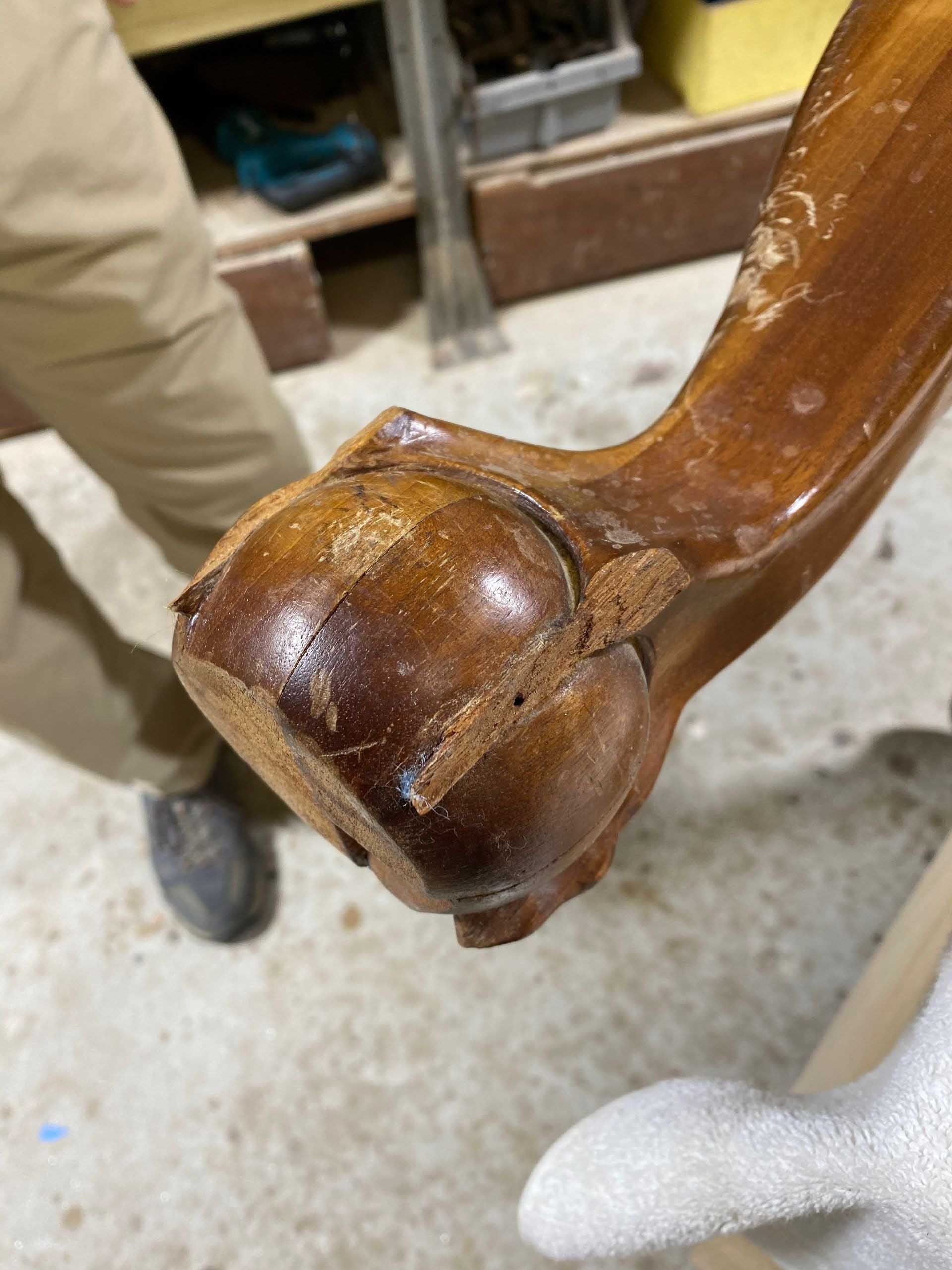 Close-up of a wooden furniture leg showing damage and repair potential. Brown wood, interior setting.