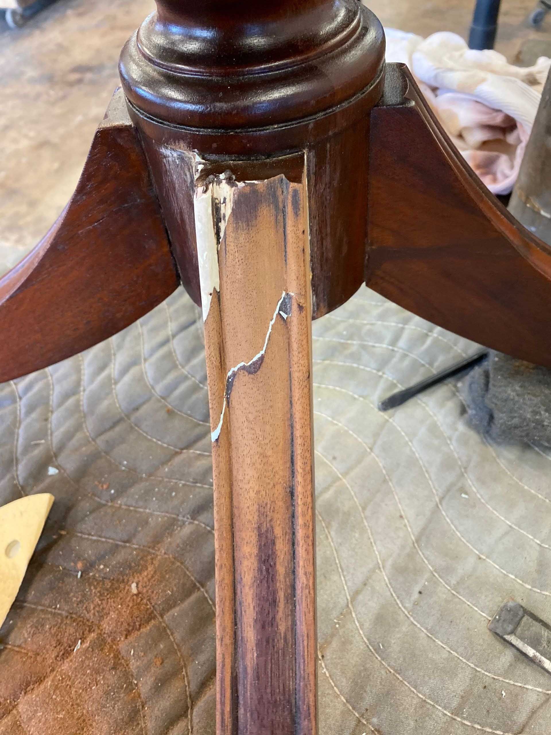 Close-up of a damaged dark wood table leg with filler visible; leg is connected to a larger base.