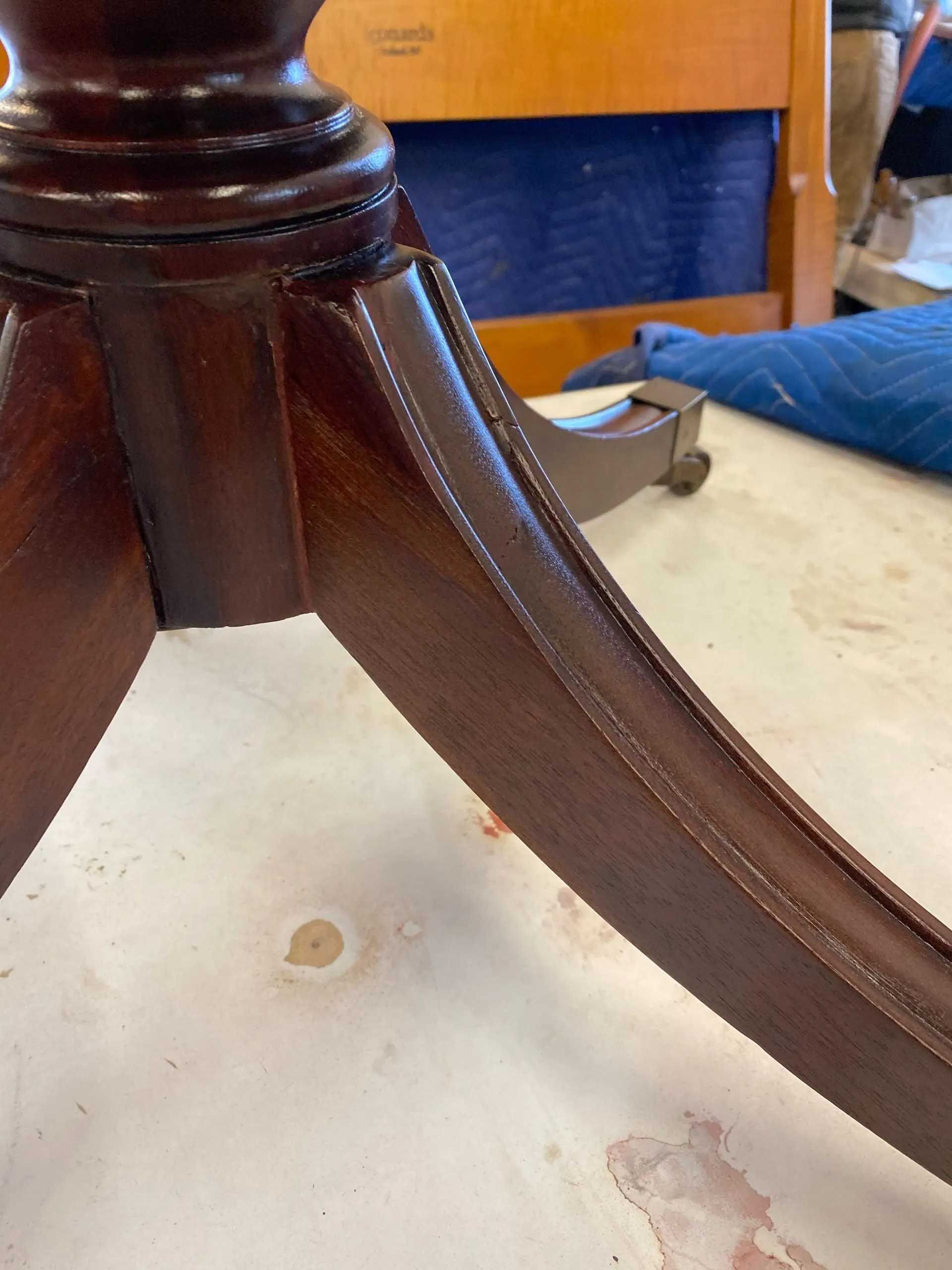 Close-up of a mahogany-colored table leg, showing carved details and attached to a pedestal base.