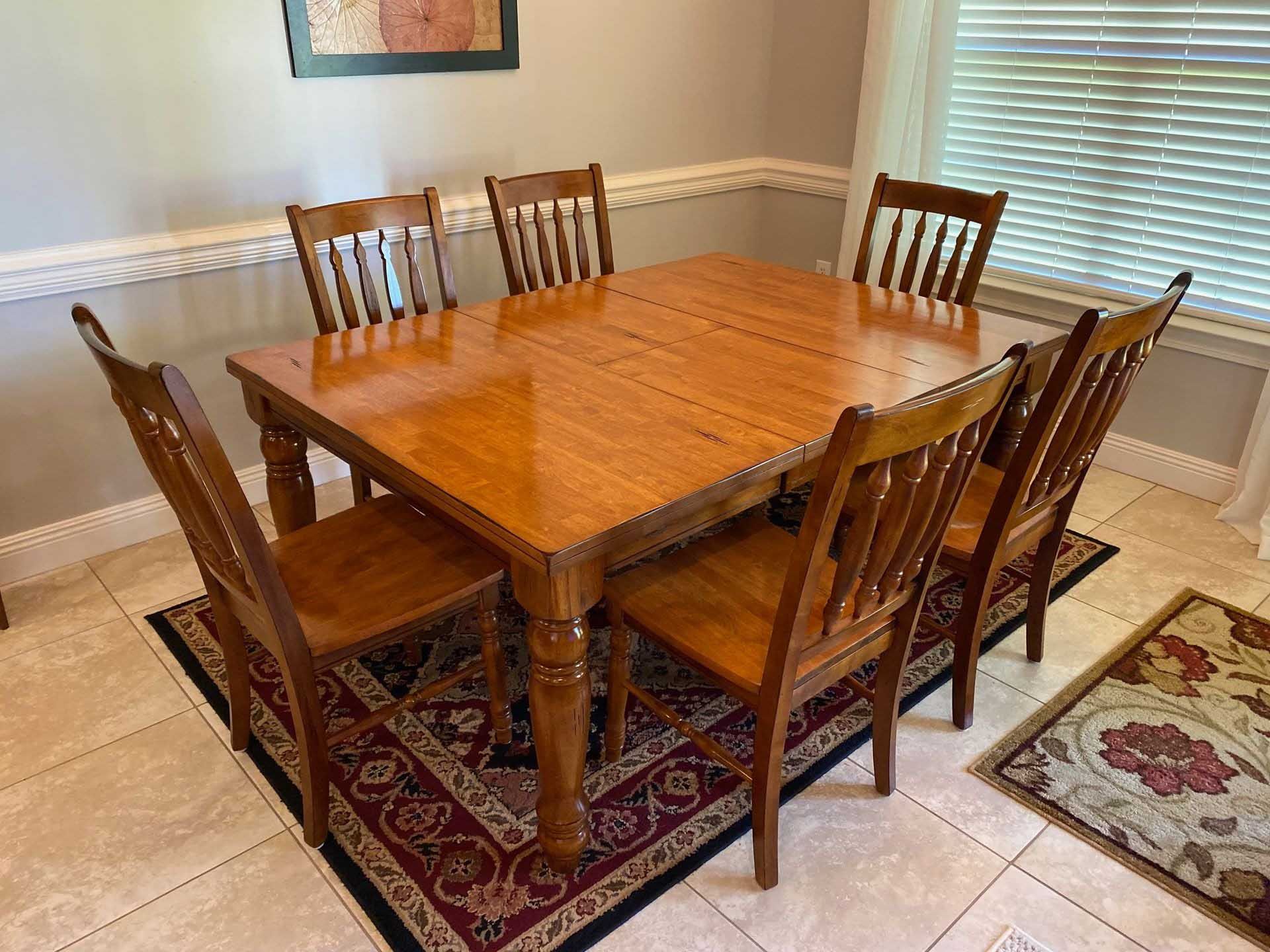 Wooden dining table with six chairs, set on a patterned rug.