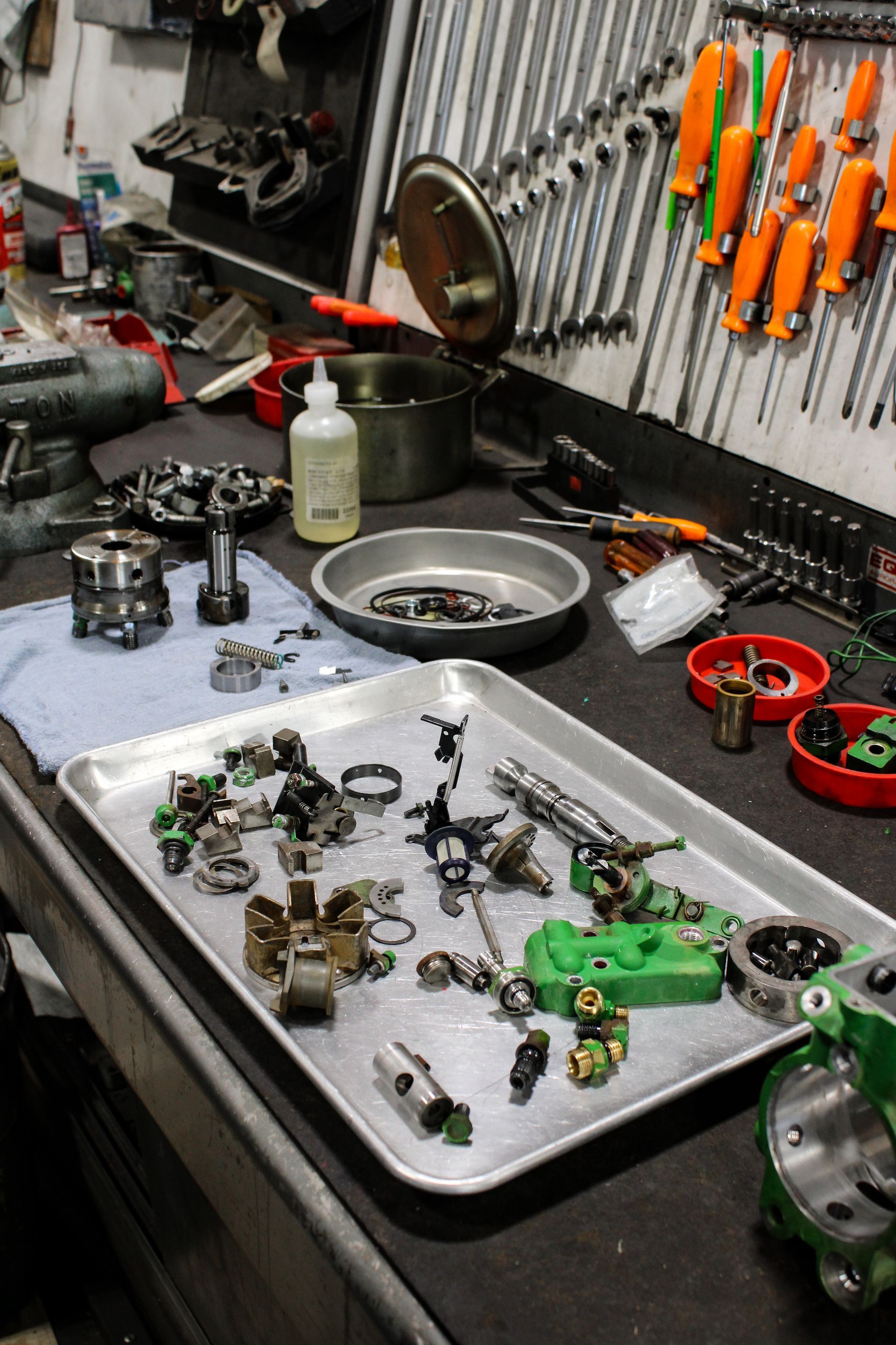 Workbench with assorted small mechanical parts, tools, and trays in a workshop.