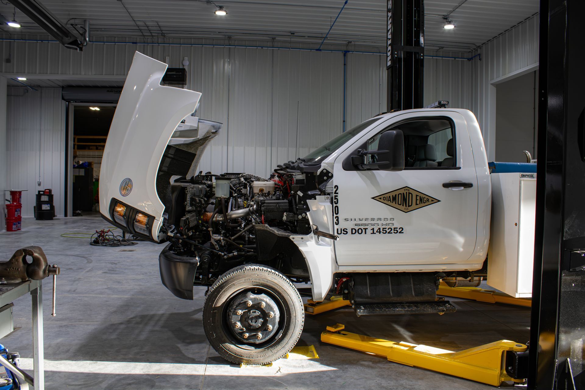 White pickup truck with front hood open in an auto shop on a lift, engine exposed
