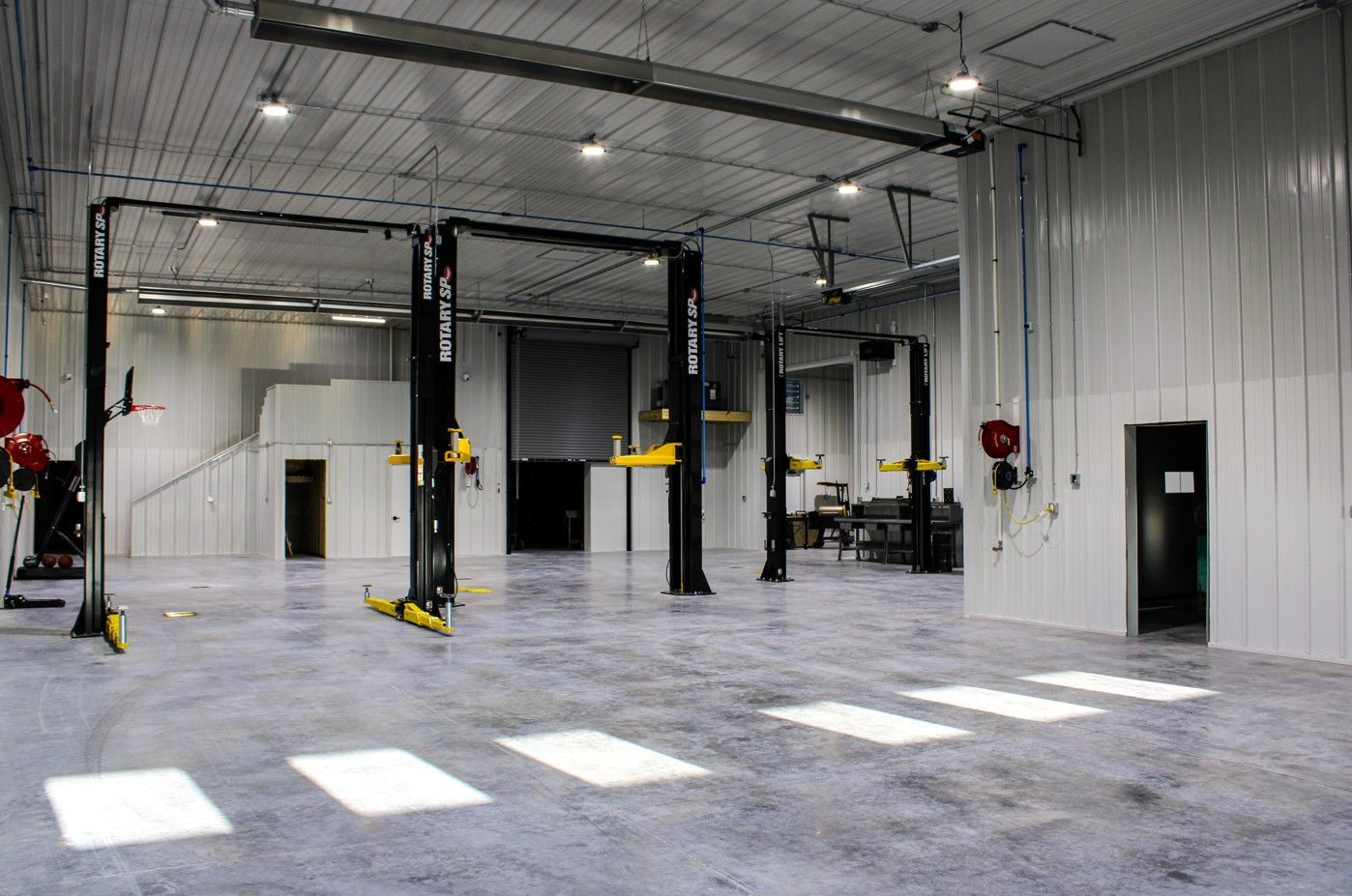 Empty auto repair garage with car lifts, a closed door, and bright light on the concrete floor