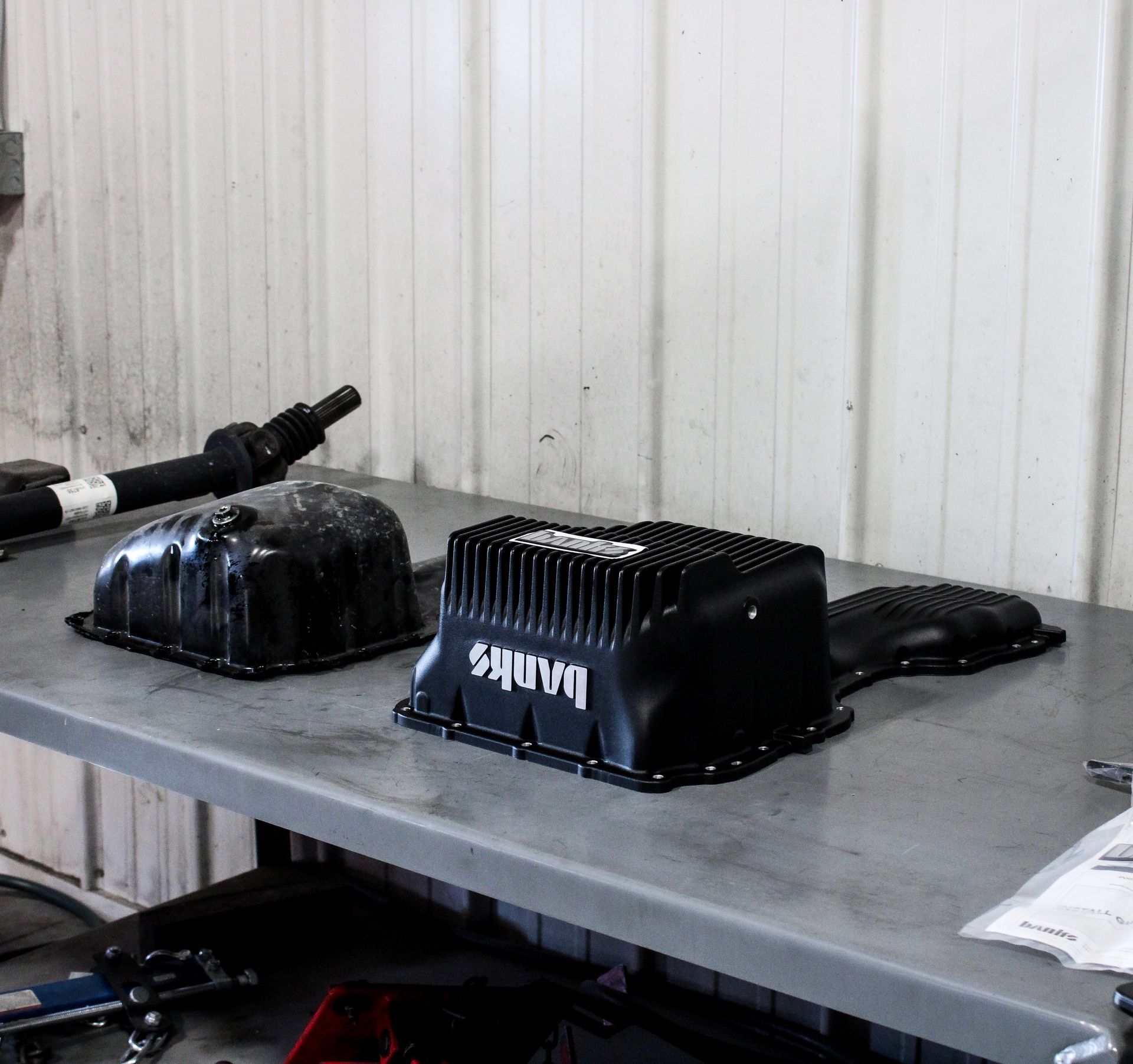 Black electronics housings on a gray workbench against a white corrugated wall.