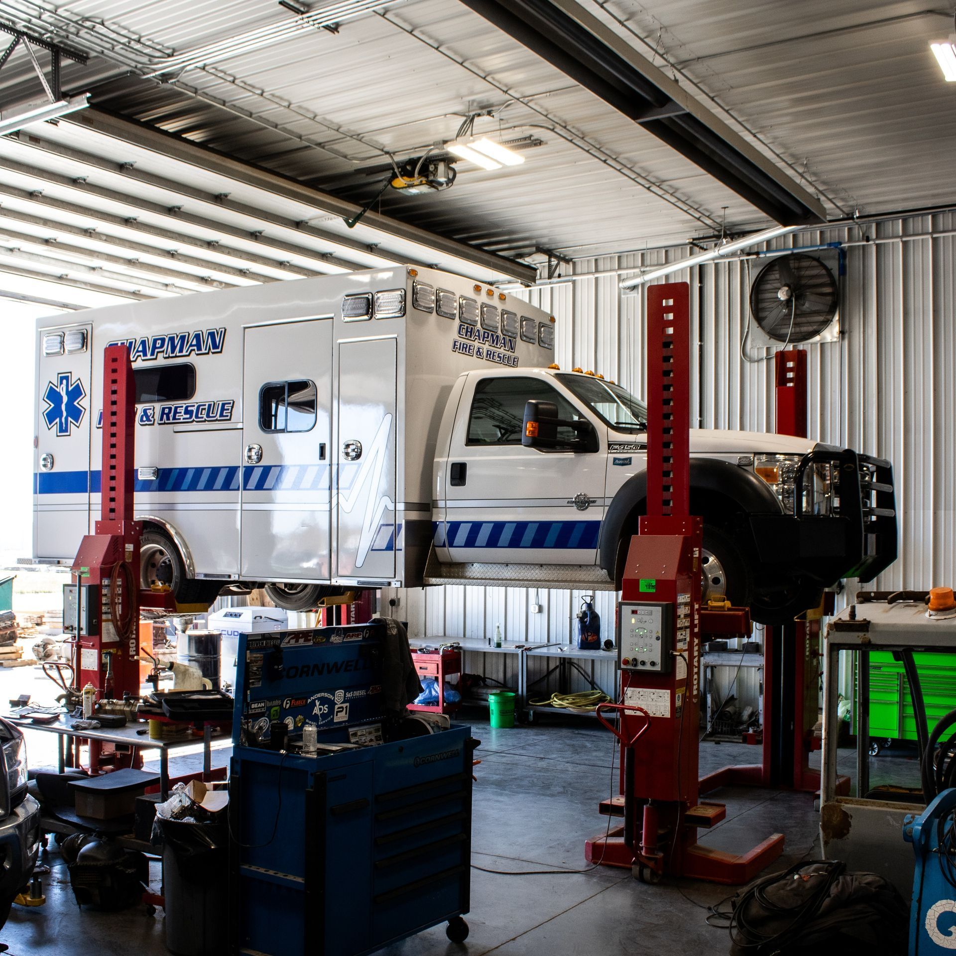 Ambulance in a garage on lifts, with equipment and tools around it.