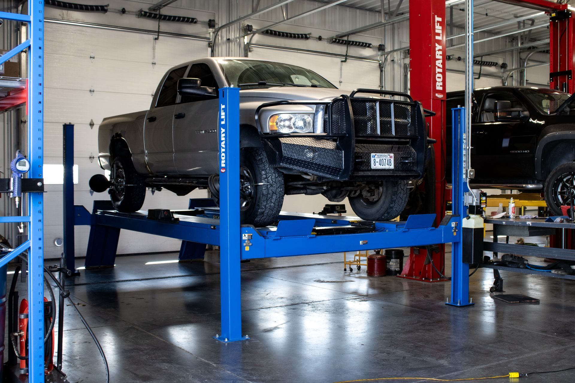 SUV on a blue hydraulic lift in an auto repair shop, with another vehicle nearby.