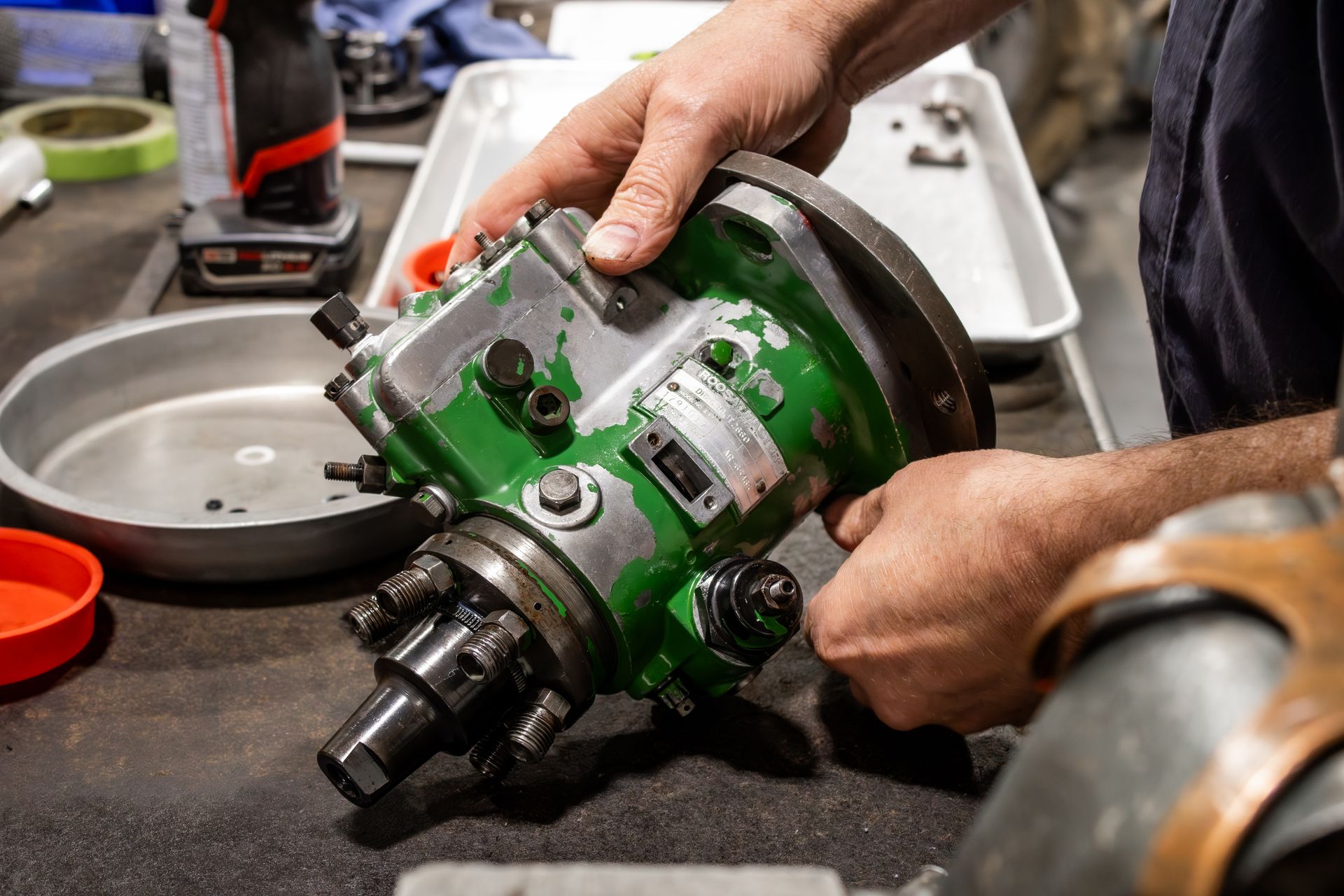 A mechanic's hands holding a green metal engine part on a workbench
