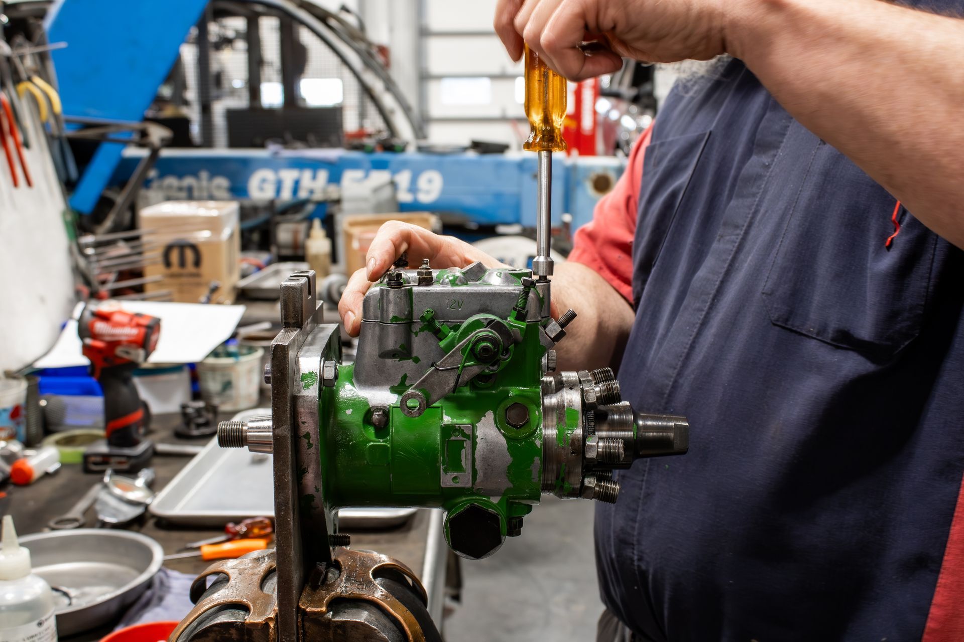 A mechanic working on a green engine in a busy auto repair shop