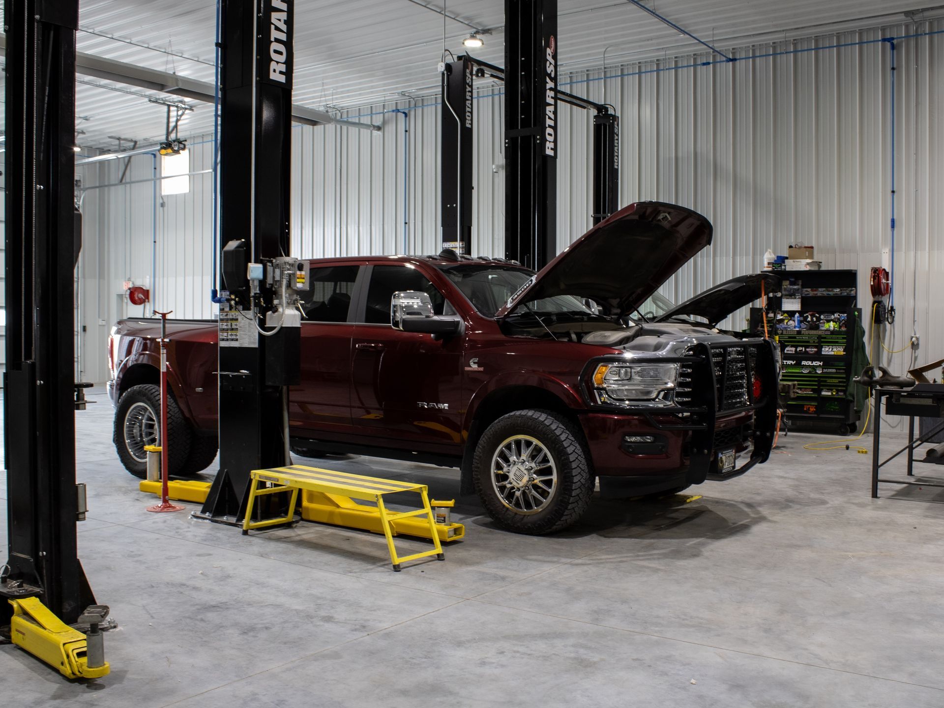 Red pickup truck in an auto shop on a lift with its hood open and a step stool nearby