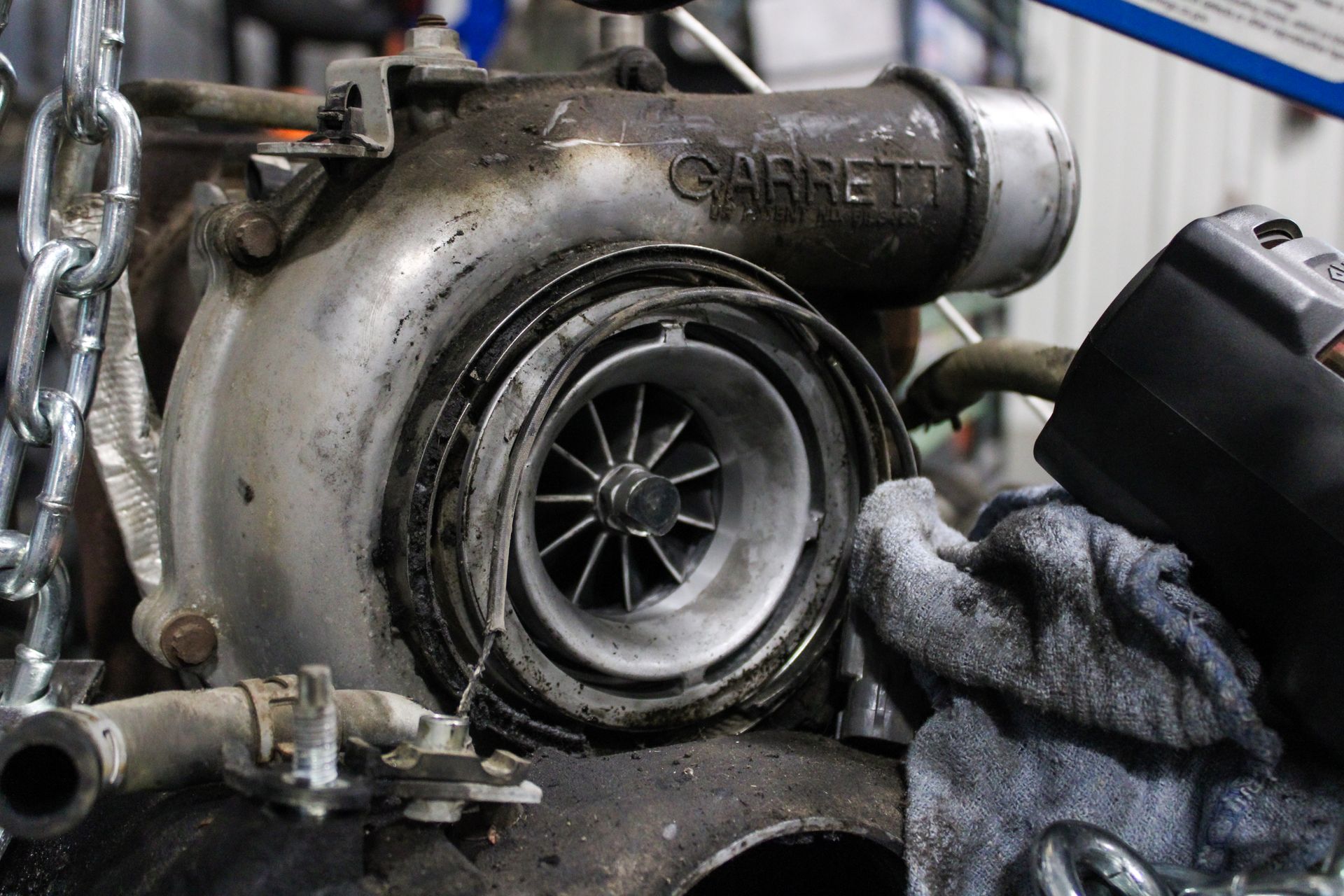 Close-up of a dirty turbocharger engine part with a rag beside it in a workshop.