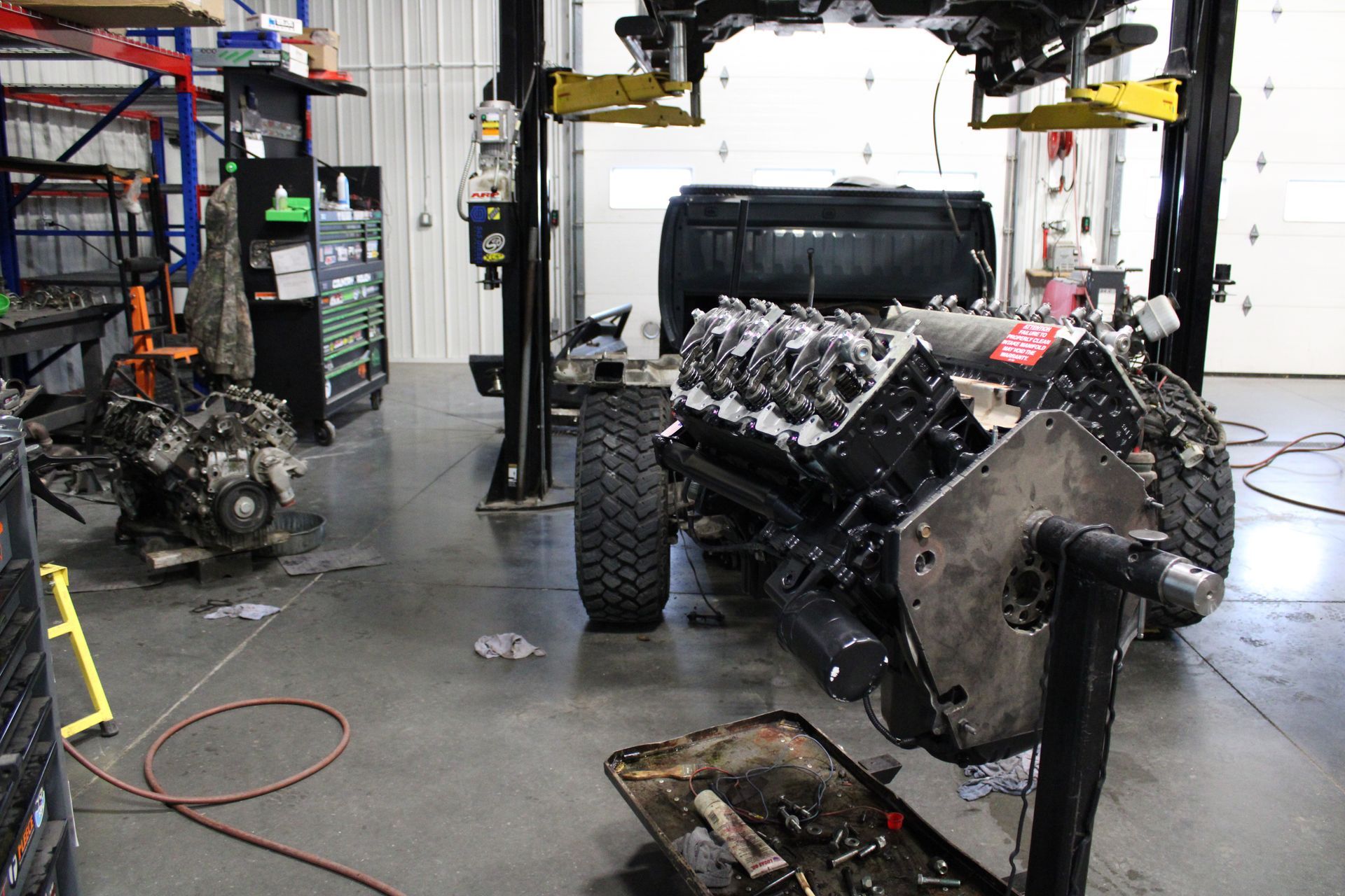 A car engine on a stand in a professional workshop, with an automotive lift and another vehicle in the background.