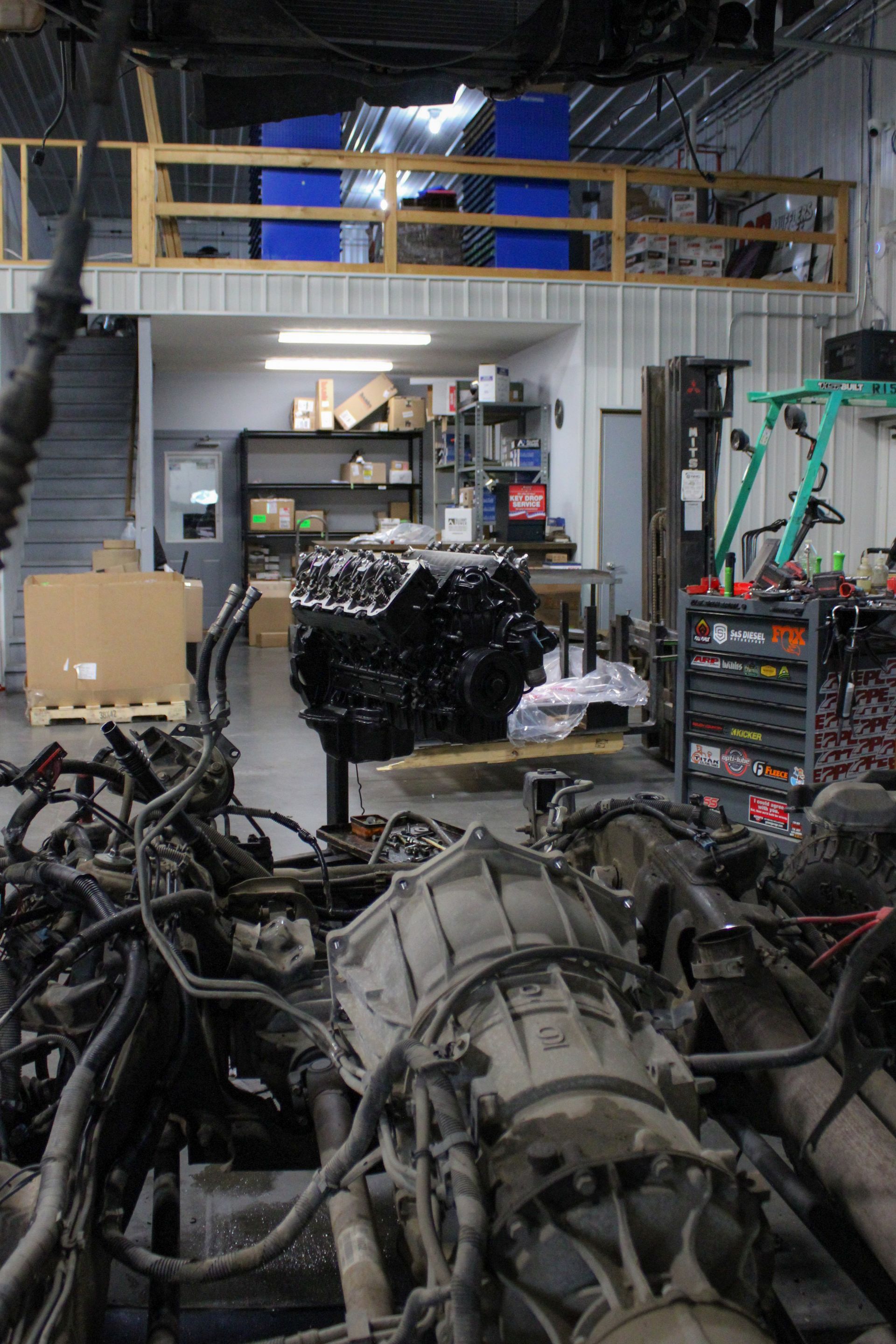 An auto repair shop interior featuring a clean black engine block on a stand, with a transmission assembly in the foreground.