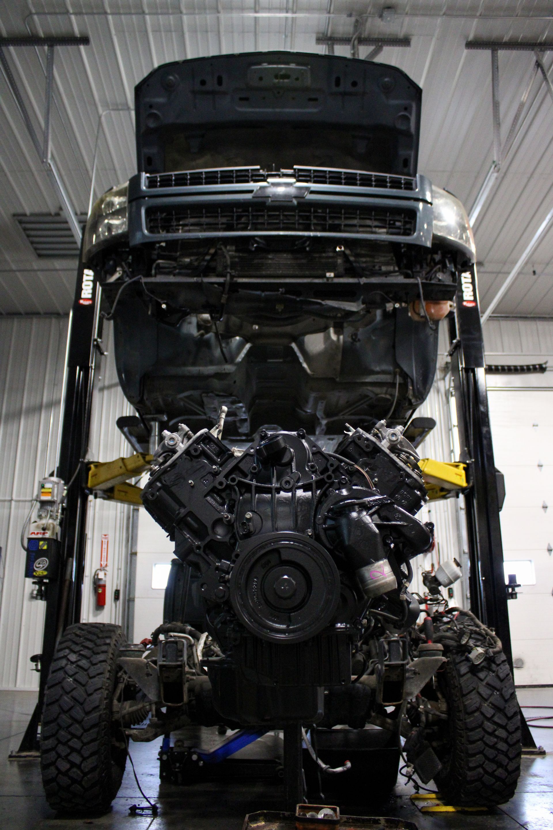 A Chevrolet truck raised on a lift in a workshop with its engine exposed and removed from the frame.