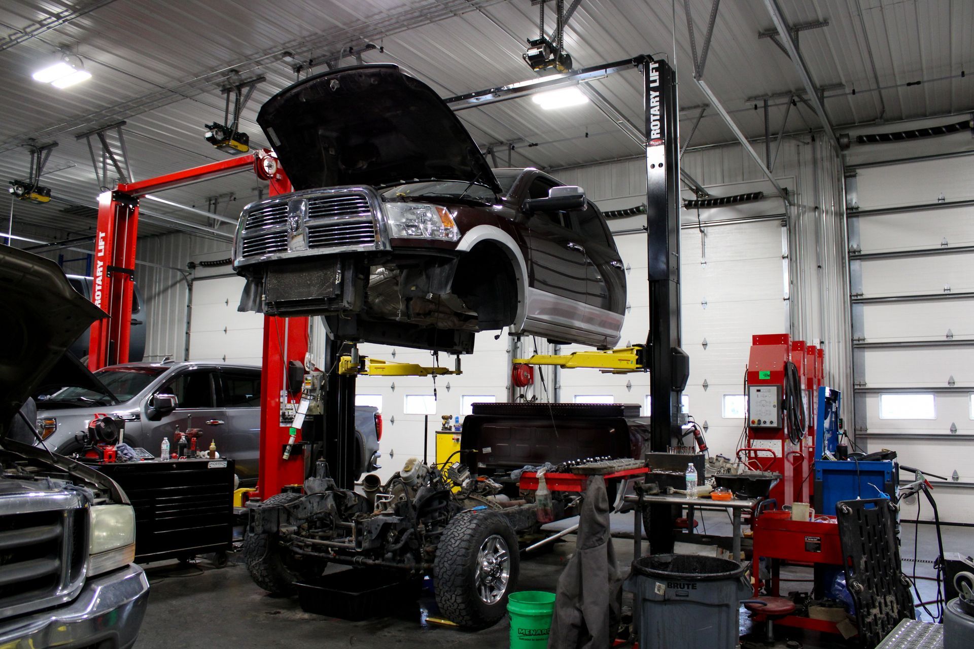 A dark pickup truck body is suspended on a hydraulic lift, separated from its chassis and wheels in an auto shop.
