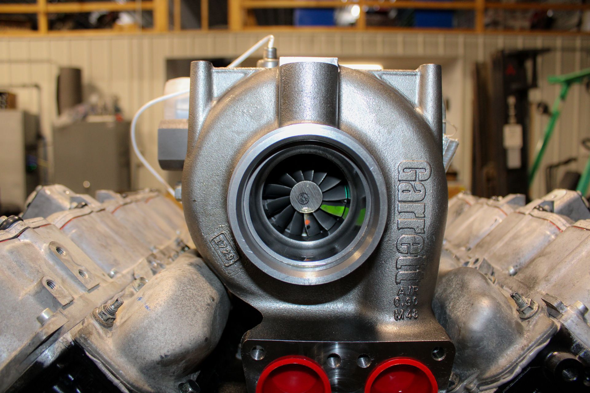 A Garrett turbocharger positioned between two engine cylinder heads inside a workshop.
