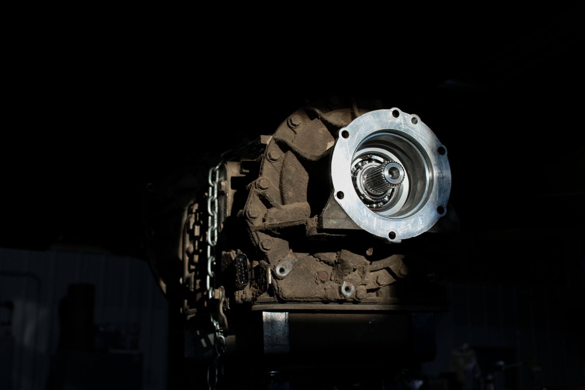 A dirty, cast-metal automotive transmission assembly shown against a dark, shadowed background.