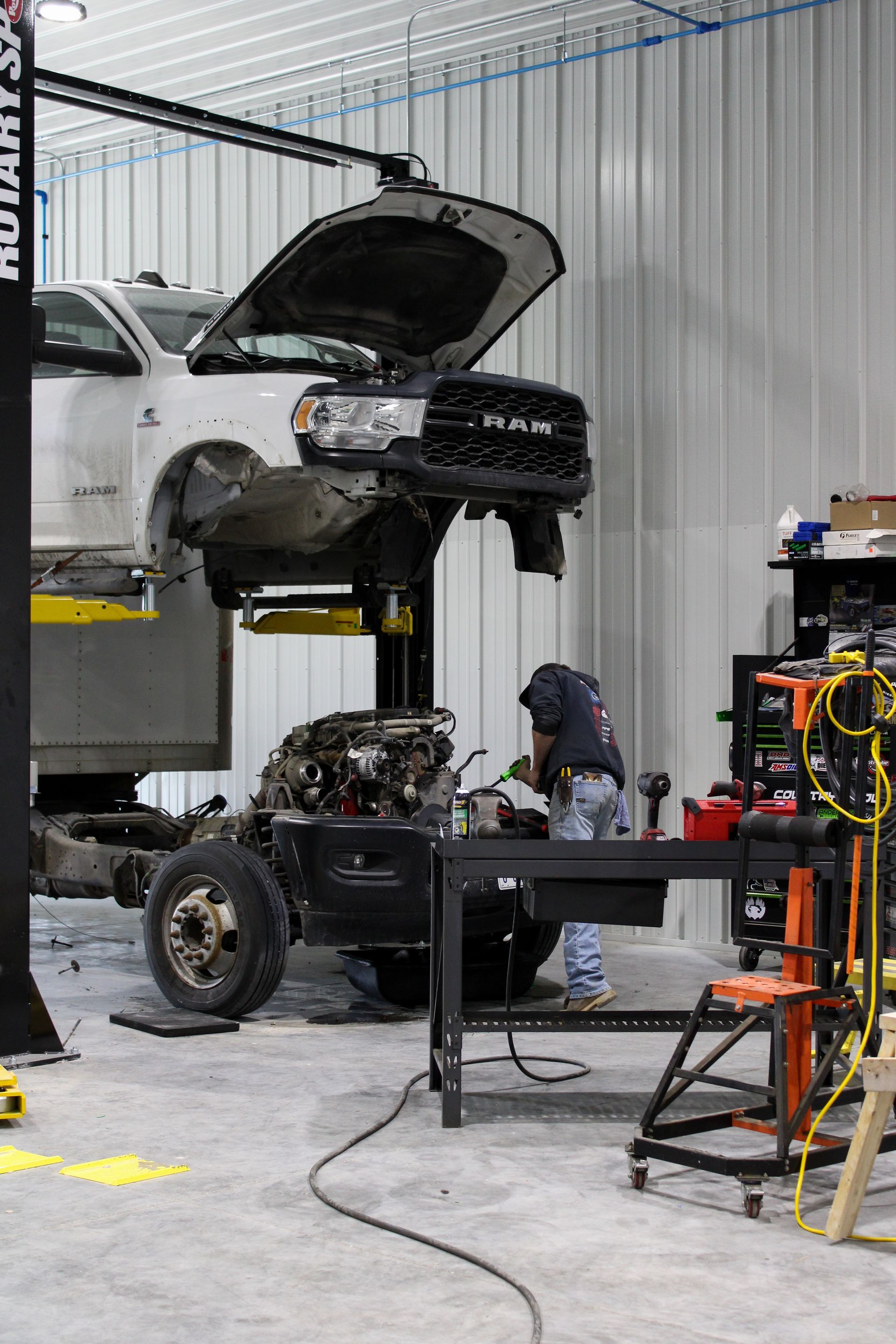 A mechanic repairs the engine of a white truck elevated on a lift inside a professional workshop.