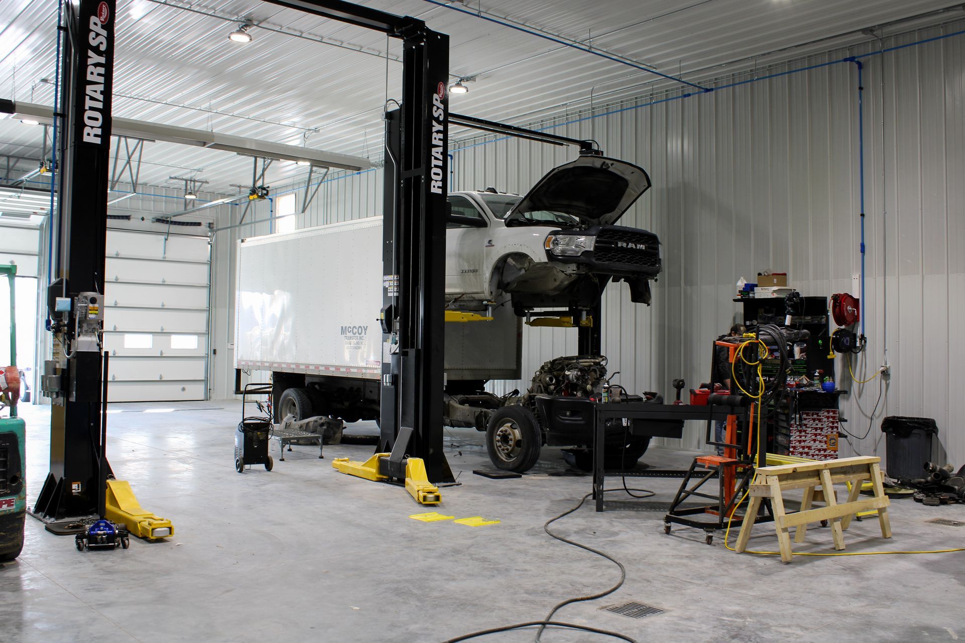 A well-lit auto repair shop with a truck lifted on a lift, exposing the chassis and engine for maintenance.