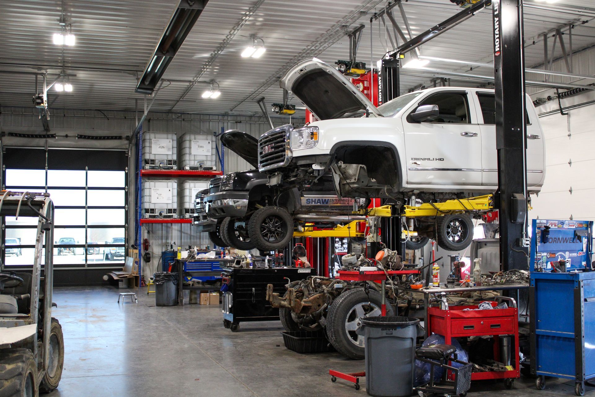 A white pickup truck elevated on a lift in a brightly lit automotive repair shop with tools and equipment nearby.