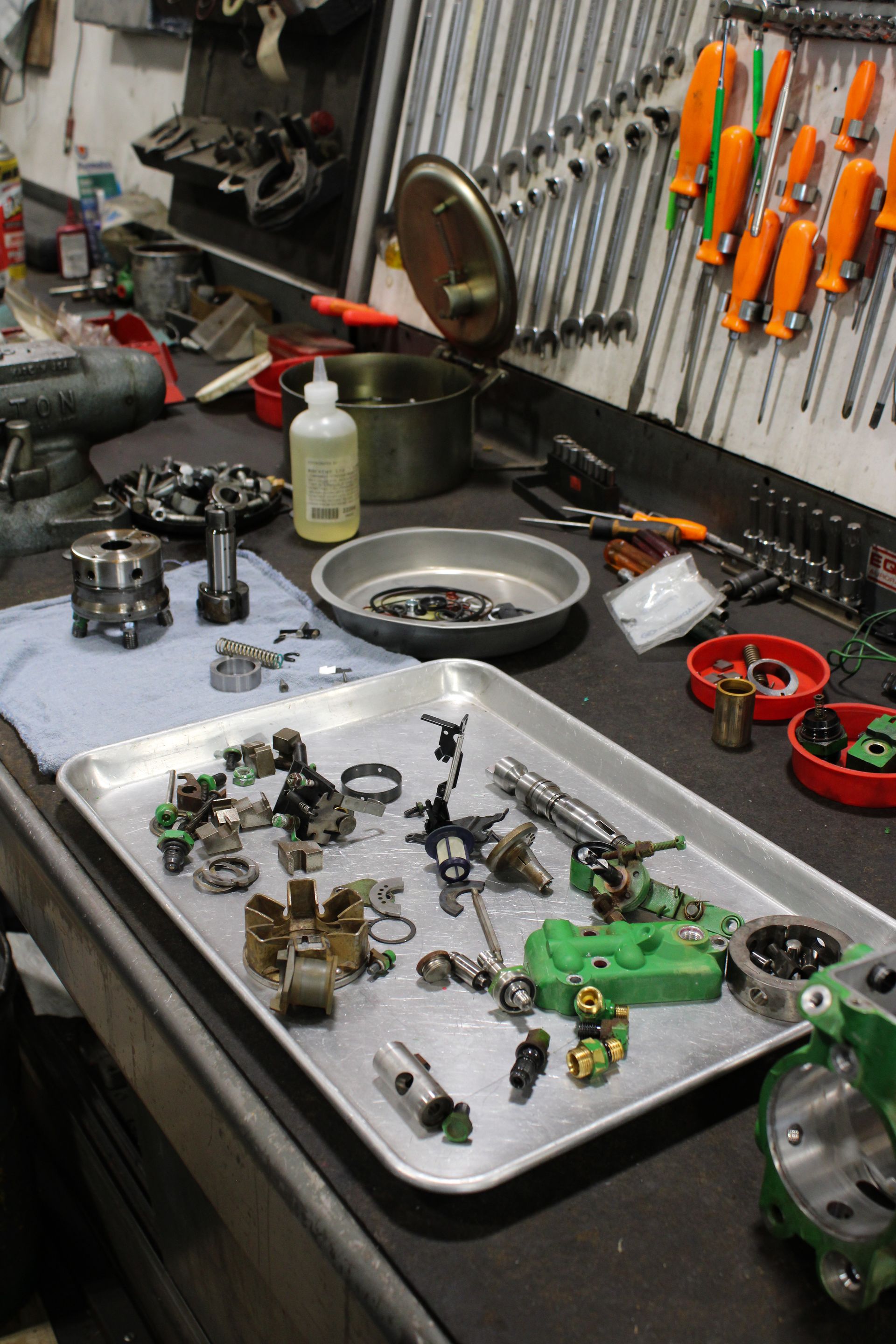 A workbench with metal parts, tools, and a tray of disassembled mechanical components in a workshop.