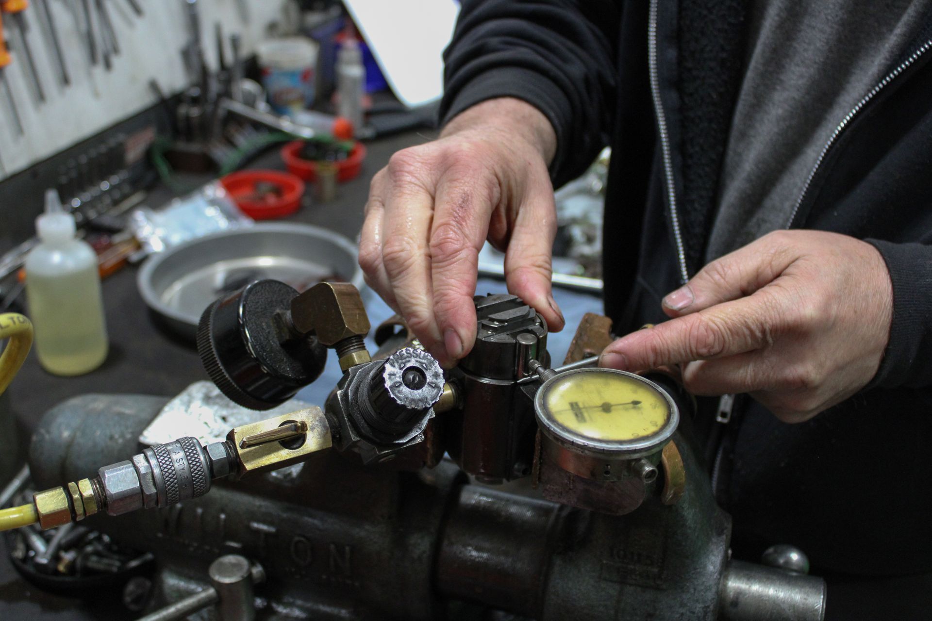 A technician adjusts a dial indicator mounted on a mechanical component secured in a bench vise in a workshop.